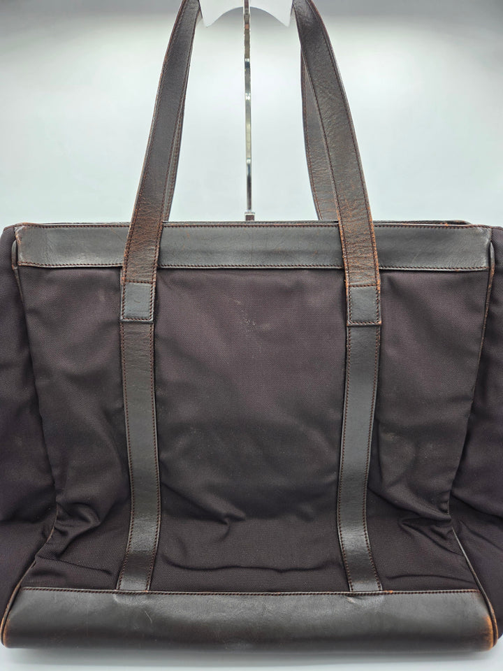 A dark brown canvas tote bag with dark brown leather shoulder straps and trim, shown from a top-down angle against a light gray background.