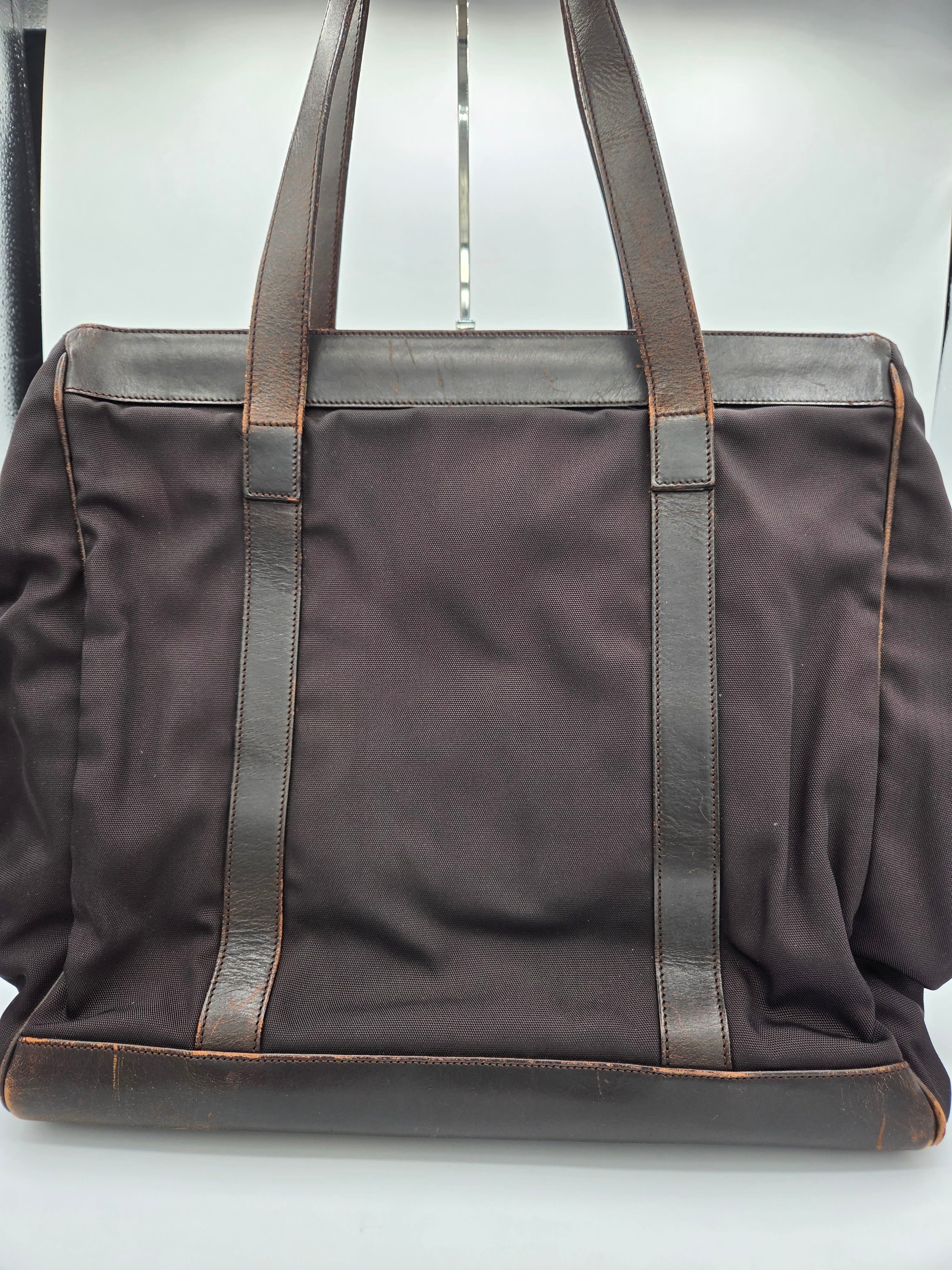 A dark brown canvas tote bag with brown leather handles and trim, shown from a top-down angle on a light gray background.
