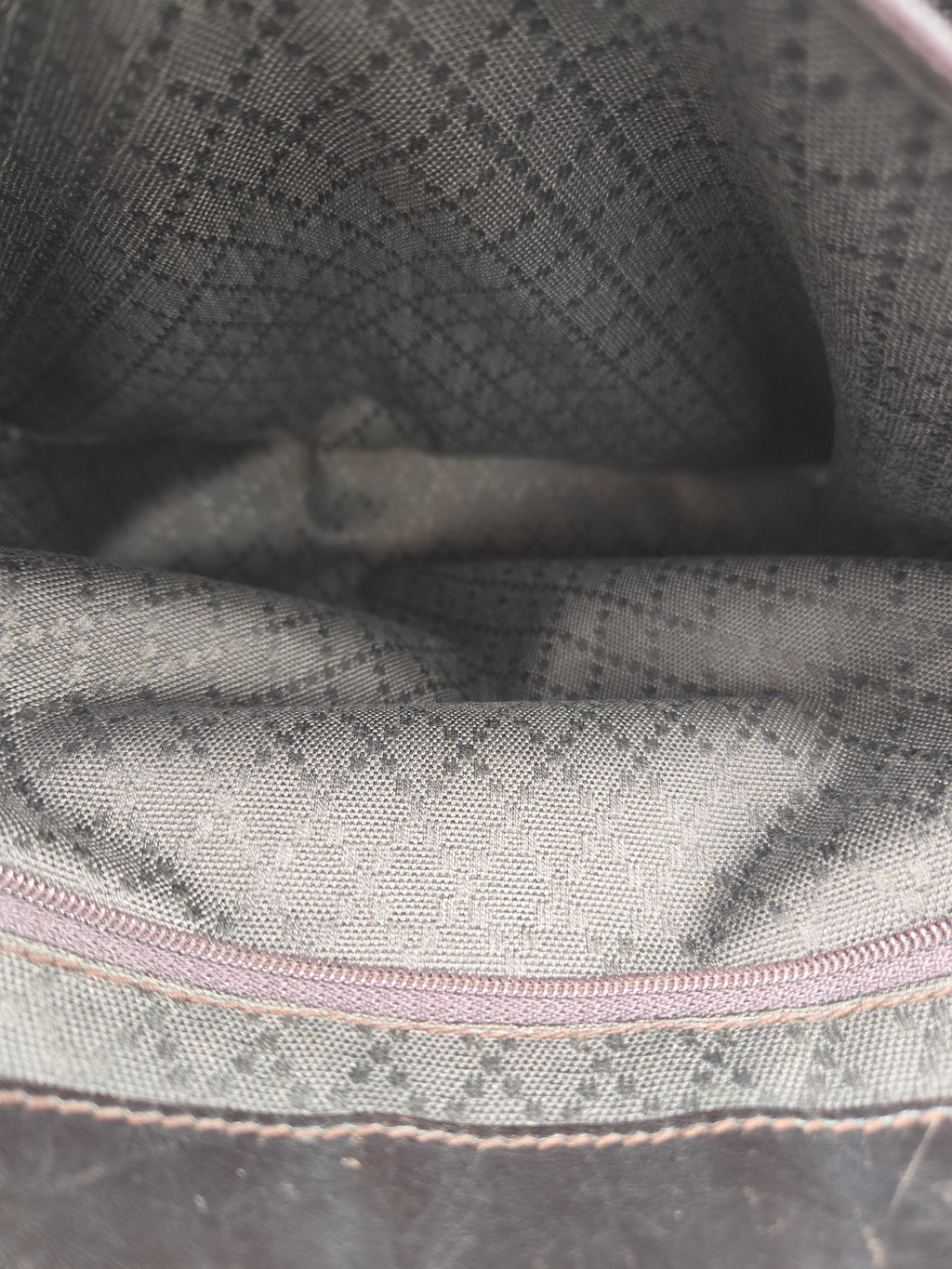 Close-up of a fabric interior with a gray and black diamond pattern, a light pink zipper, and beige stitching.