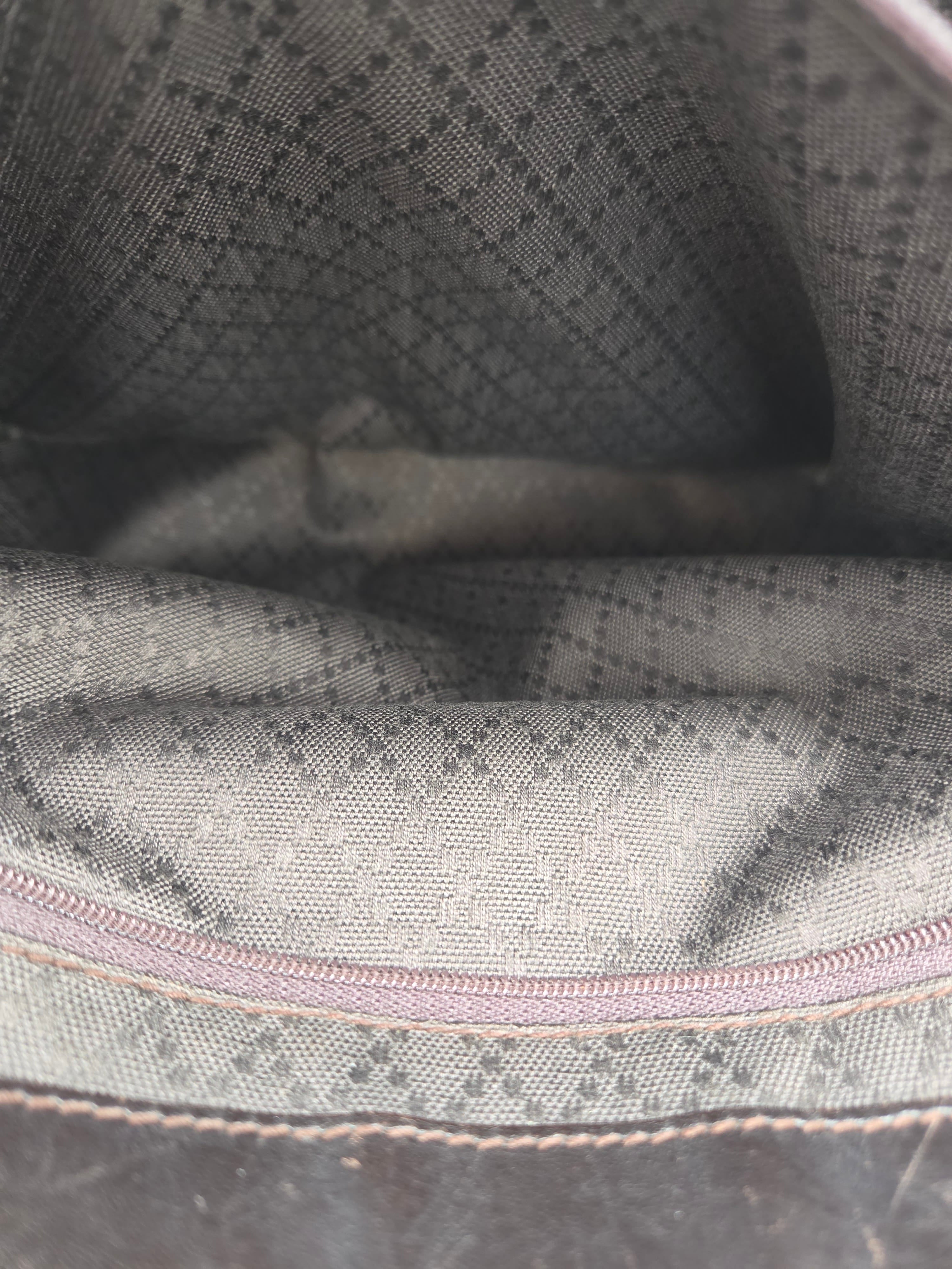 Close-up of a fabric interior with a gray and black diamond pattern, a light pink zipper, and beige stitching.