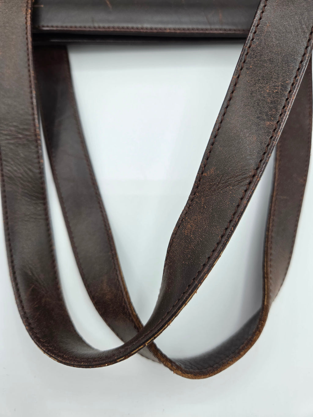 A close-up of a dark brown leather strap with visible grain and neat stitching, arranged in loops against a plain white background.