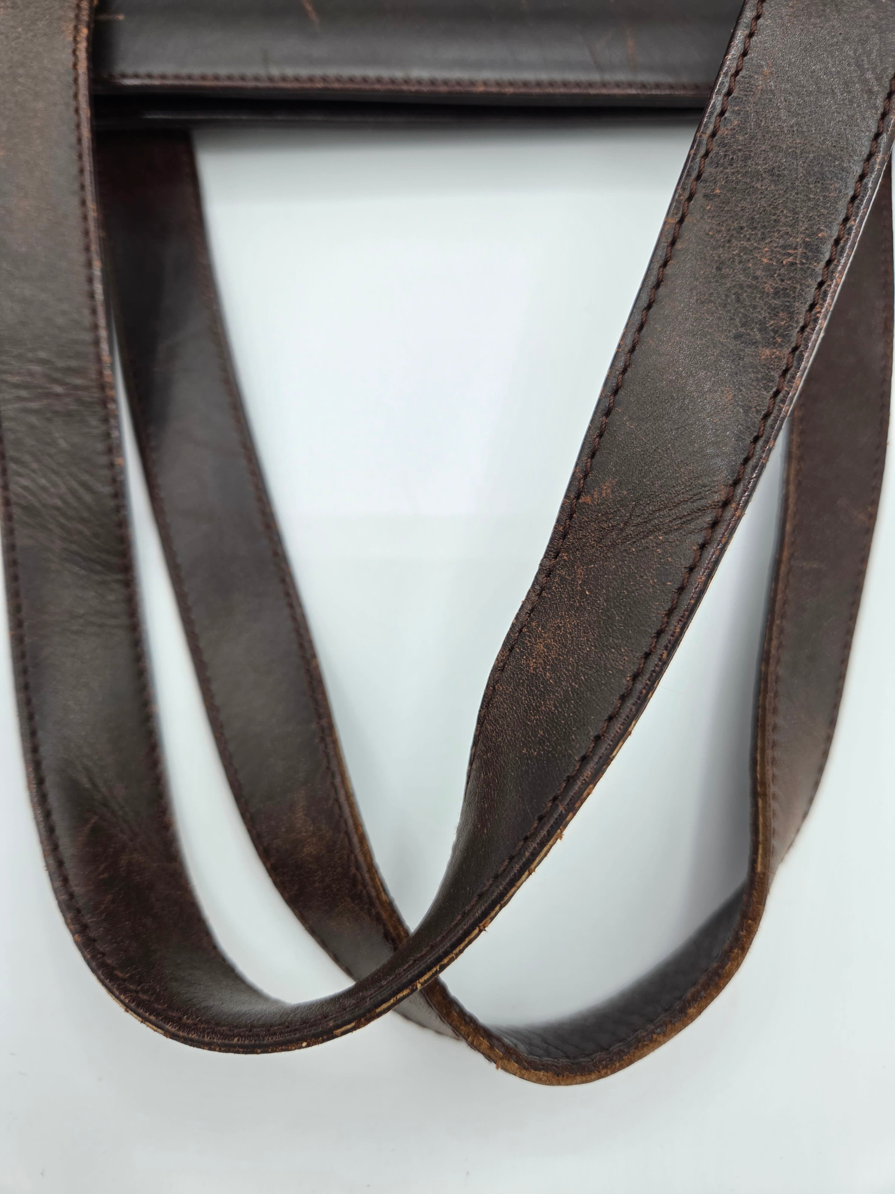 A close-up of a dark brown leather strap with visible grain and neat stitching, arranged in loops against a plain white background.