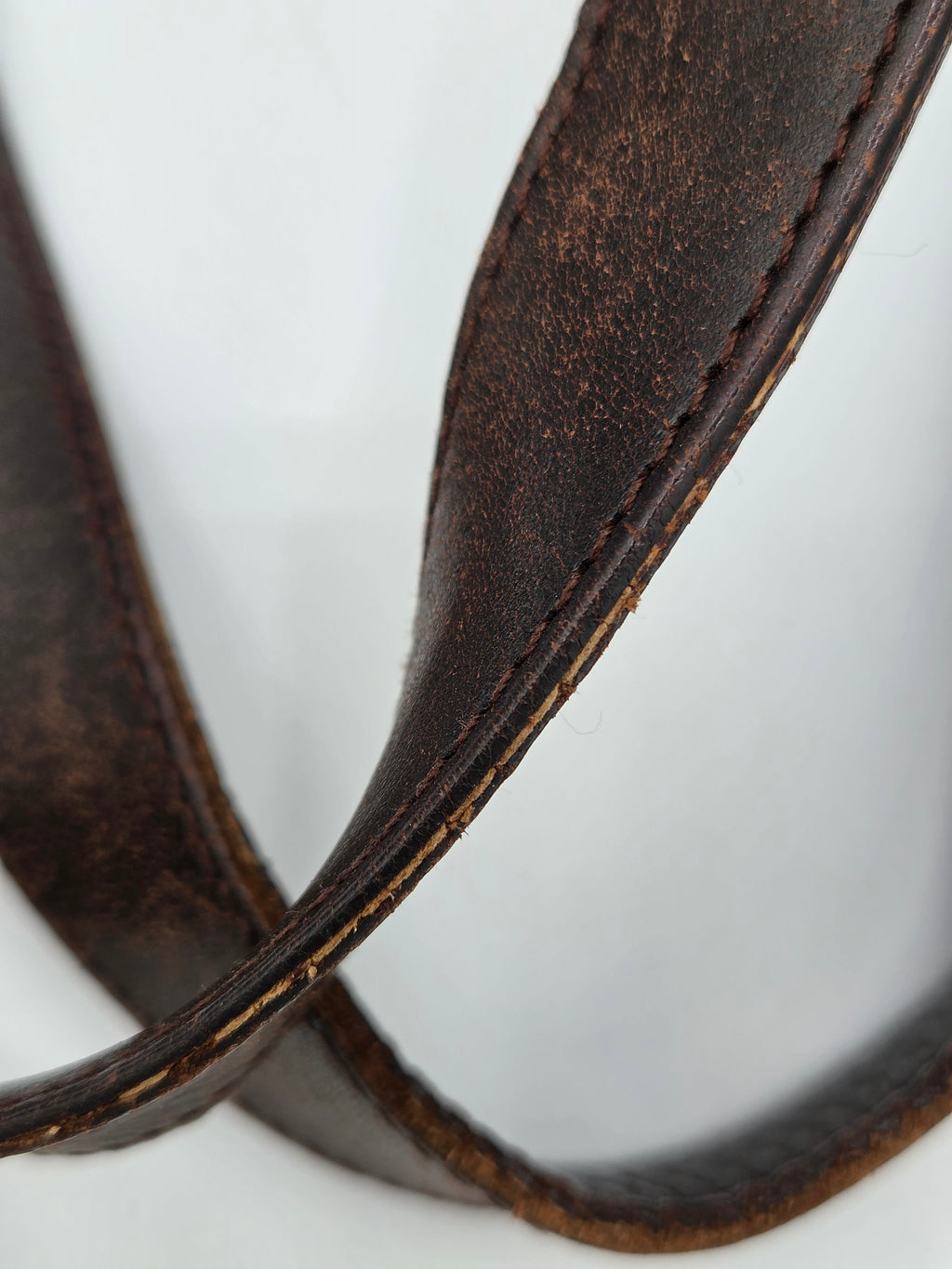 A close-up of a dark brown leather strap, likely a camera strap or belt, showing the texture and stitching against a plain white background.