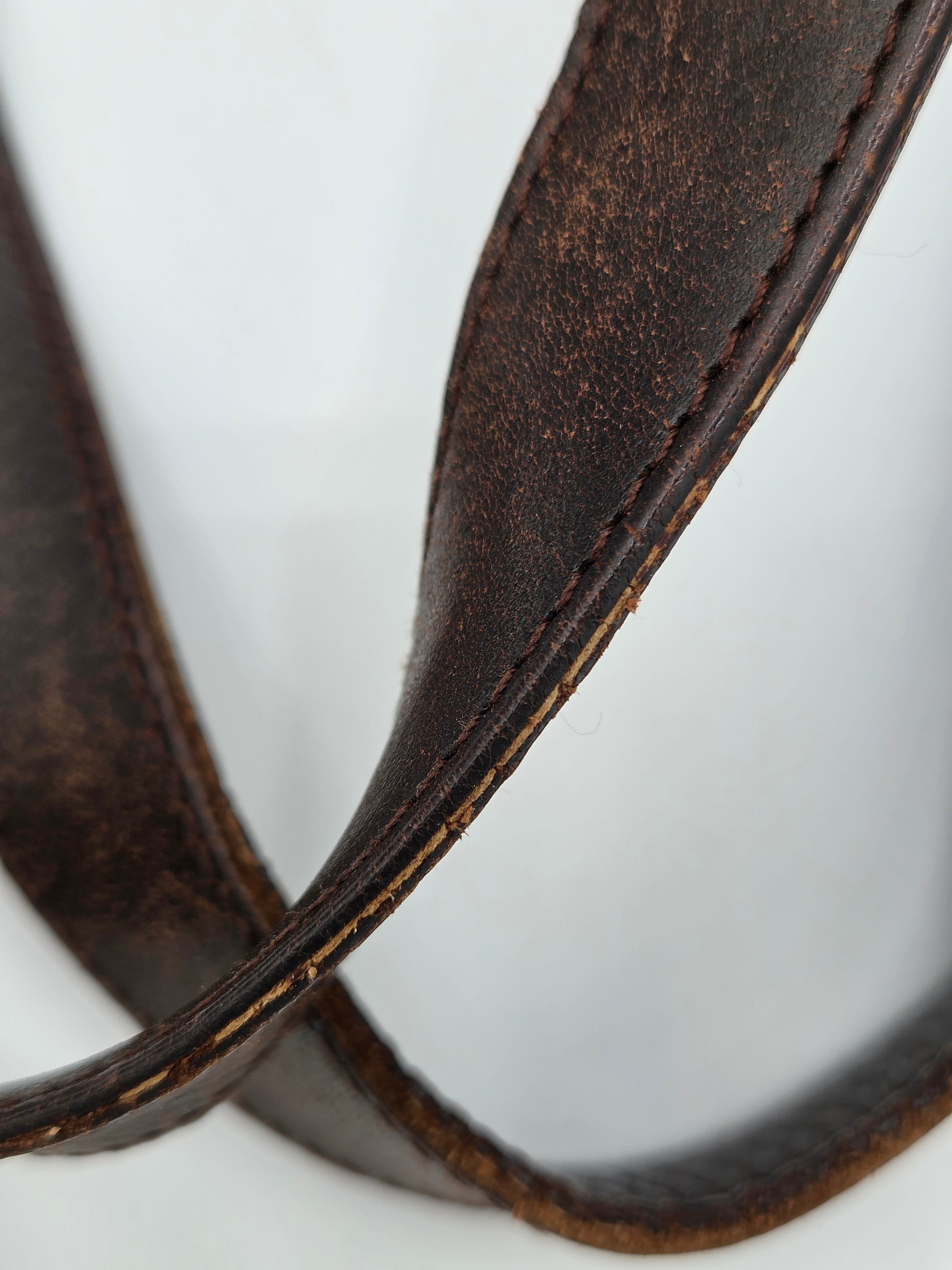 A close-up of a dark brown leather strap, likely a camera strap or belt, showing the texture and stitching against a plain white background.