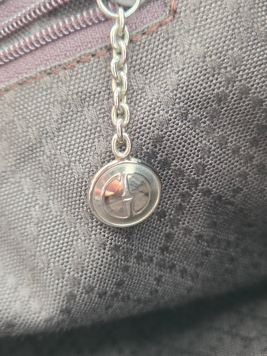 Close-up of a silver-tone metal chain and round clasp attached to a gray woven fabric surface.