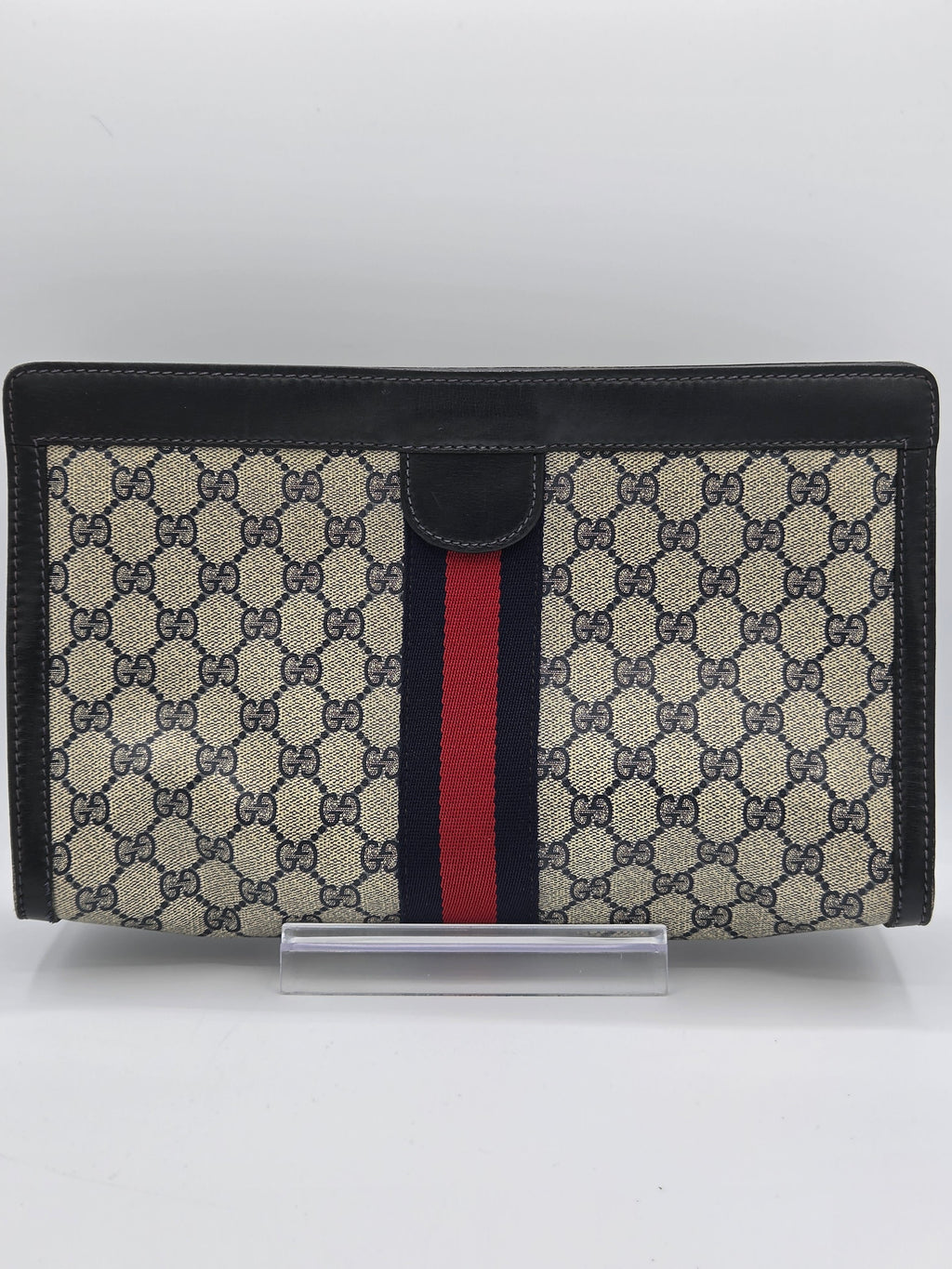 A Gucci monogram canvas document holder or wallet with black leather trim and a signature red and navy green web stripe, shown standing upright against a plain white background.