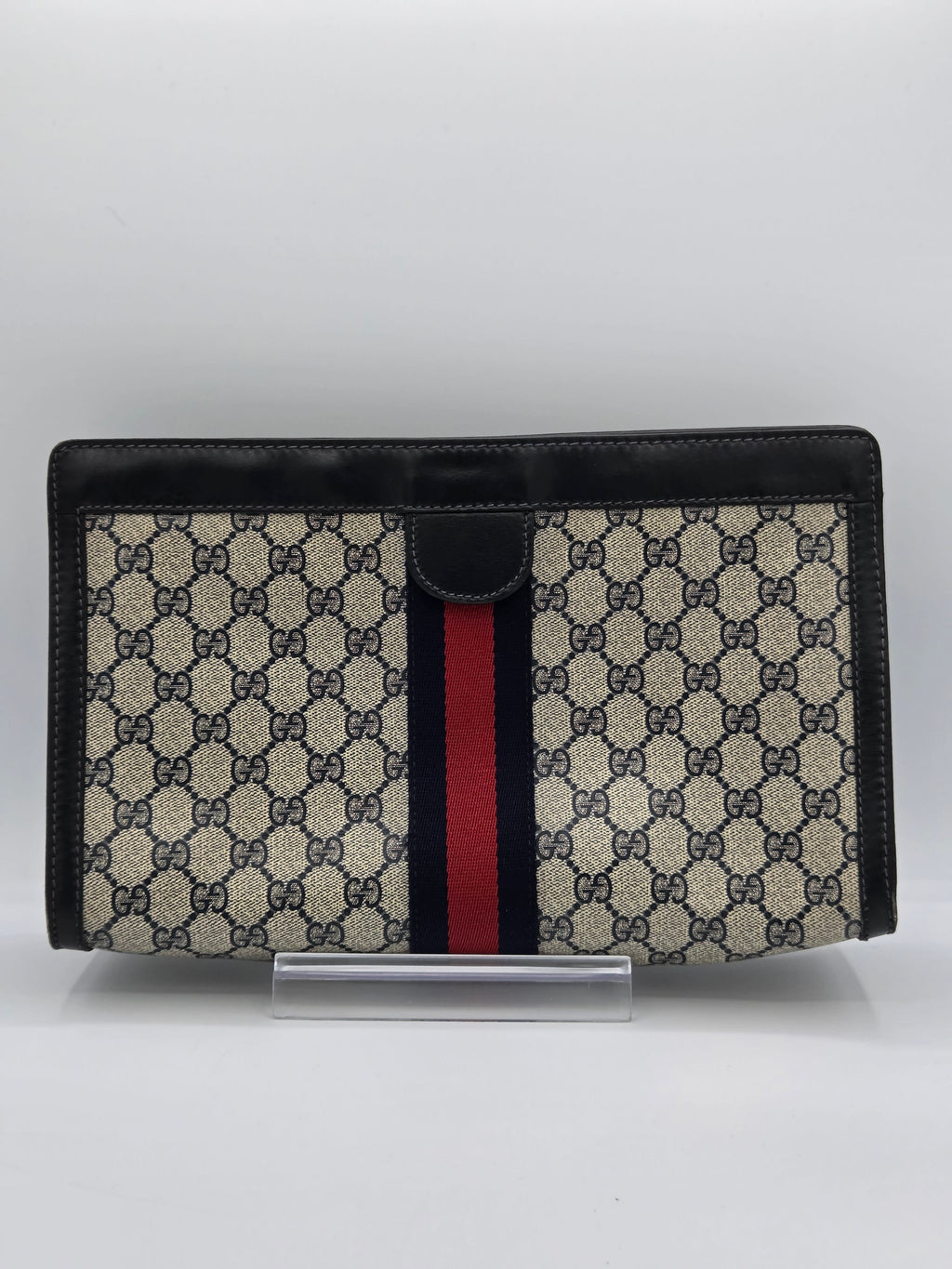 A Gucci monogram canvas document pouch with black leather trim and a signature red and navy green web stripe, shown on a light gray background.