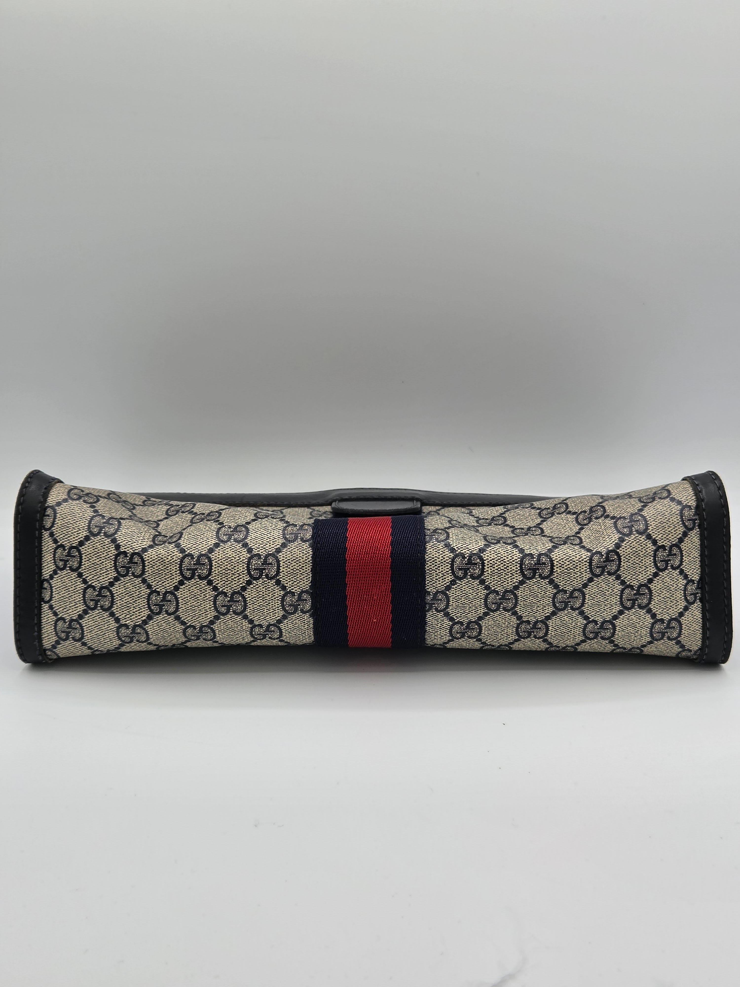 A Gucci sleeve featuring the brand's signature GG Supreme monogram pattern in beige and black, with a classic green and red web stripe down the center, and black trim.