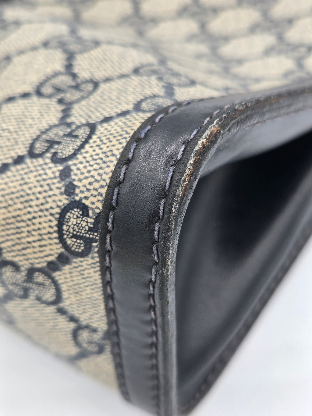 Close-up of a Gucci monogram canvas bag corner with dark brown leather trim and visible wear on the edge.