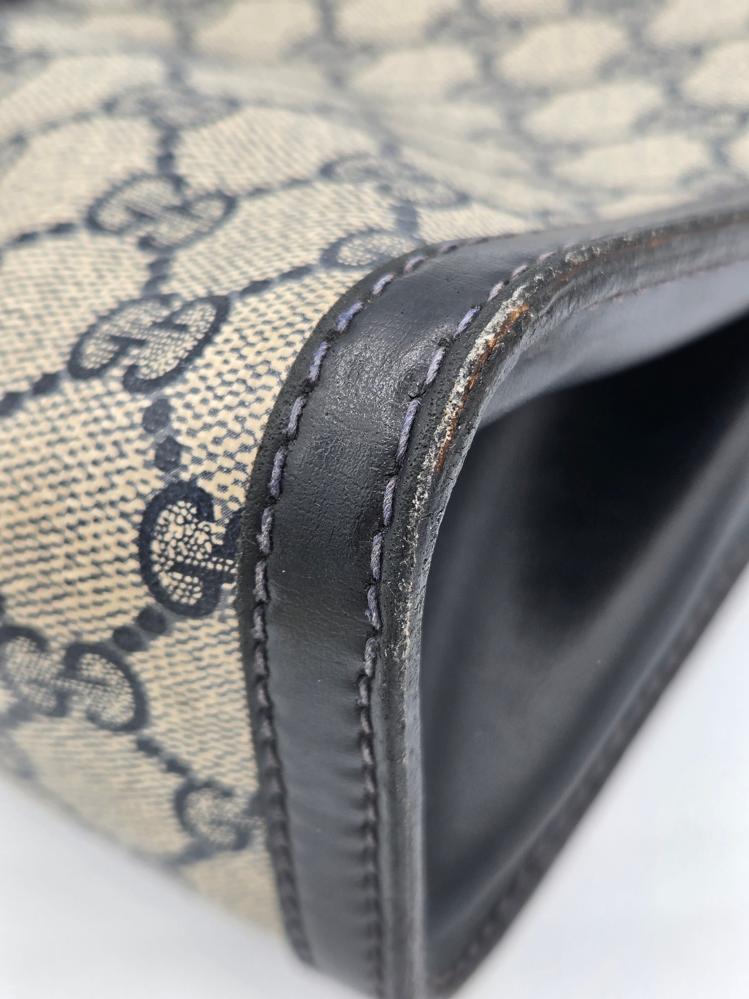 Close-up of a Gucci monogram canvas bag corner with dark brown leather trim and visible wear on the edge.