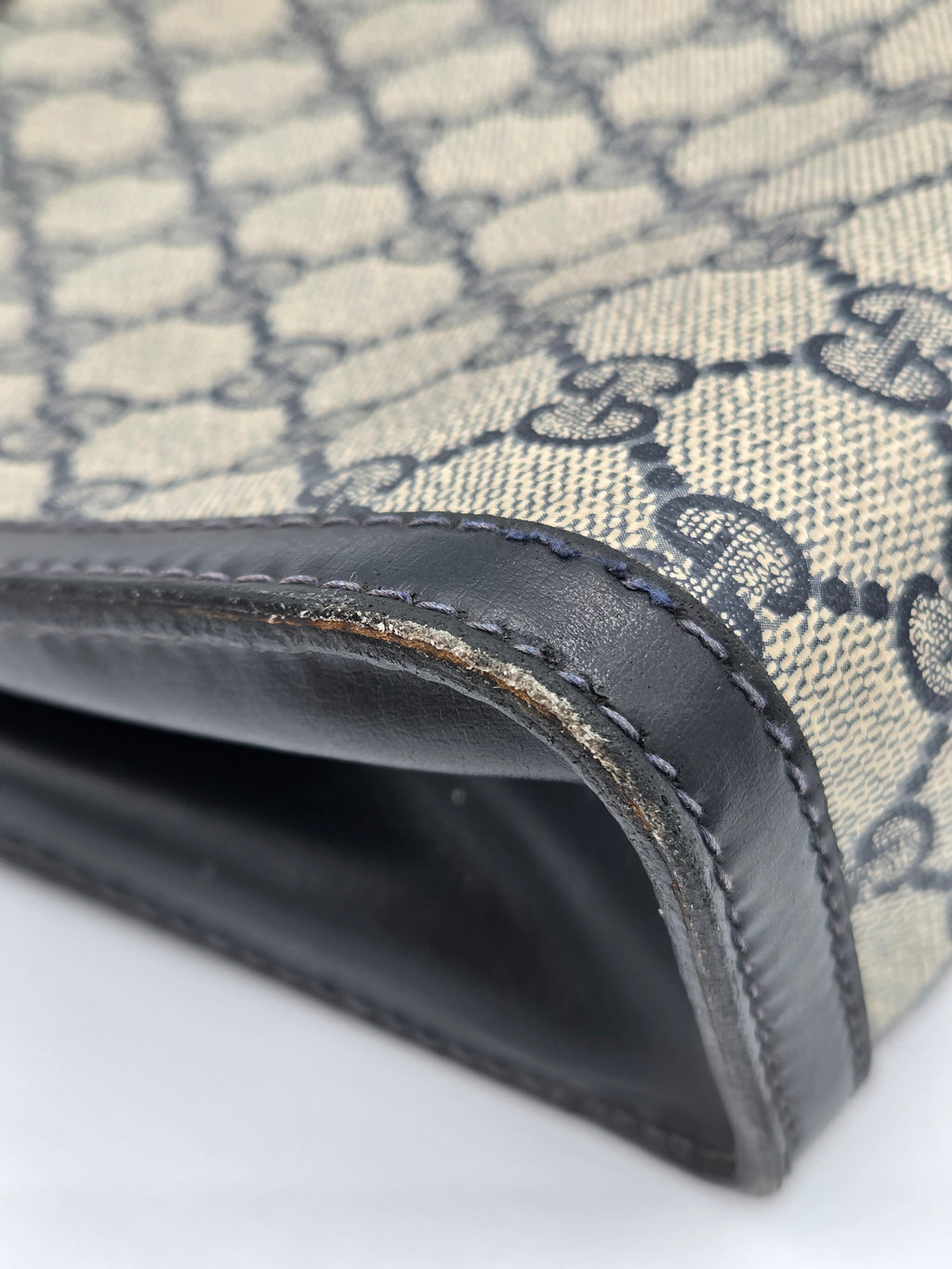 Close-up of a Gucci monogram canvas wallet or clutch showing the beige and gray GG pattern, black leather trim, and stitching.