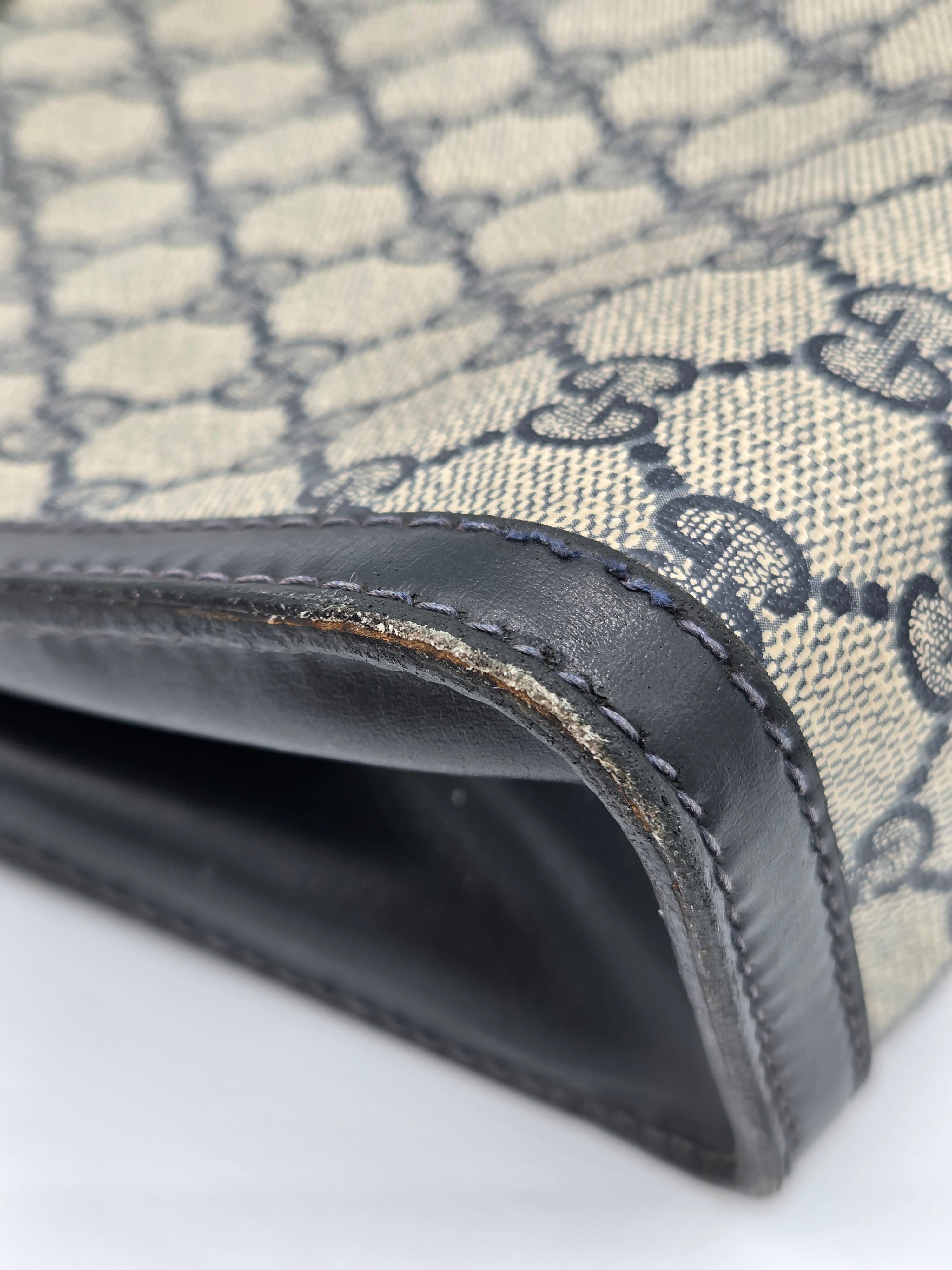 Close-up of a Gucci monogram canvas wallet or clutch showing the beige and gray GG pattern, black leather trim, and stitching.