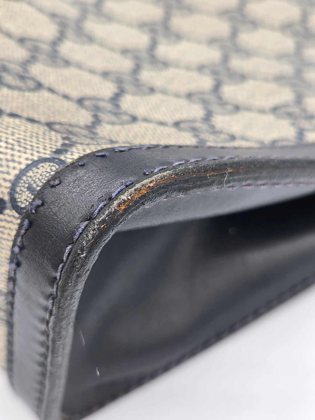 Close-up of a Gucci monogram canvas bag corner with dark brown leather trim and visible wear, showing the interior lining and stitching.
