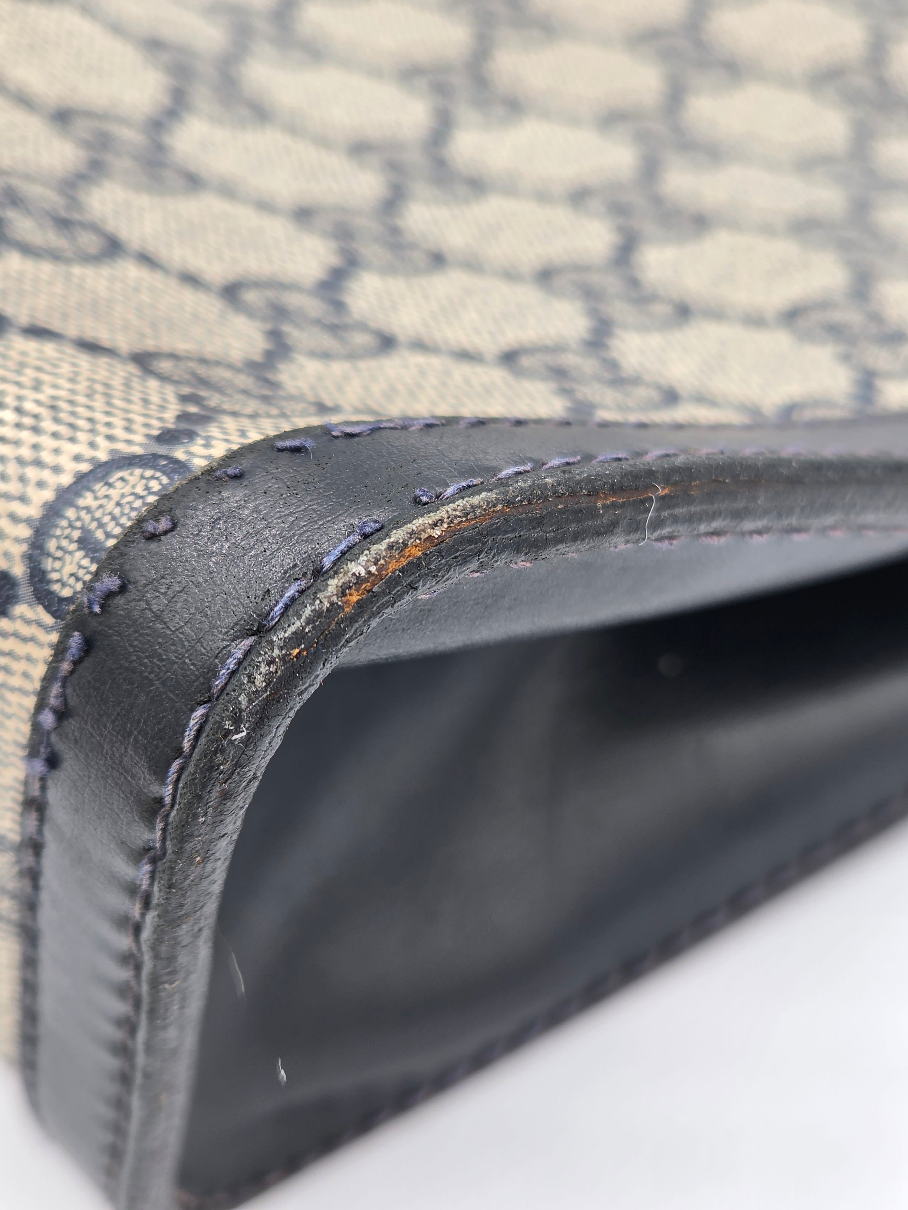 Close-up of a Gucci monogram canvas bag corner with dark brown leather trim and visible wear, showing the interior lining and stitching.