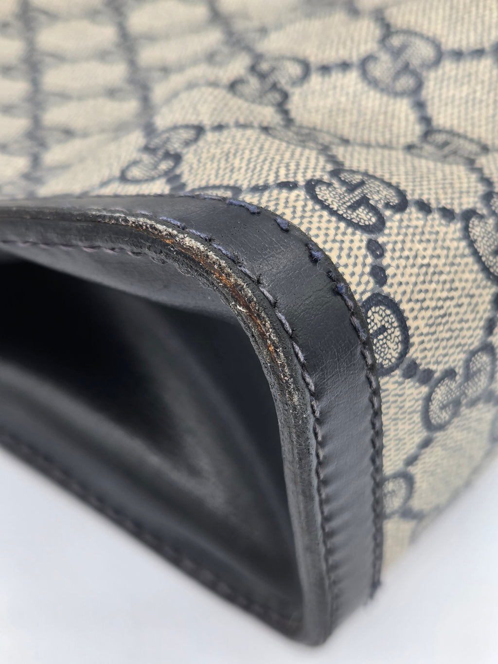 Close-up of a Gucci monogram canvas and black leather trim on a wallet or pouch, showing the classic interlocking GG pattern and a worn edge of the leather.