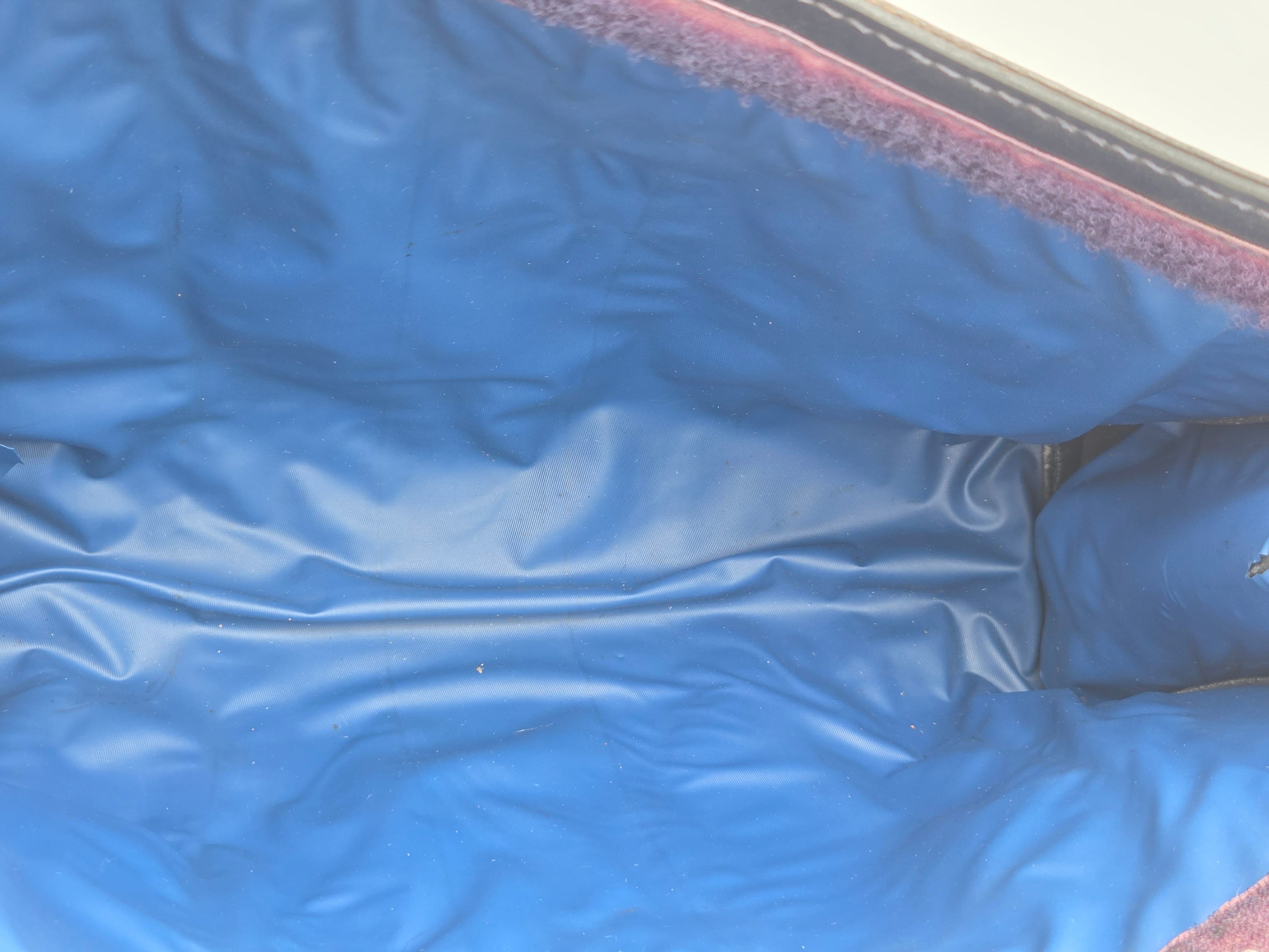 Close-up of a blue vinyl or plastic cover with a textured, slightly wrinkled surface and a dark reddish-brown fuzzy trim along the edge.