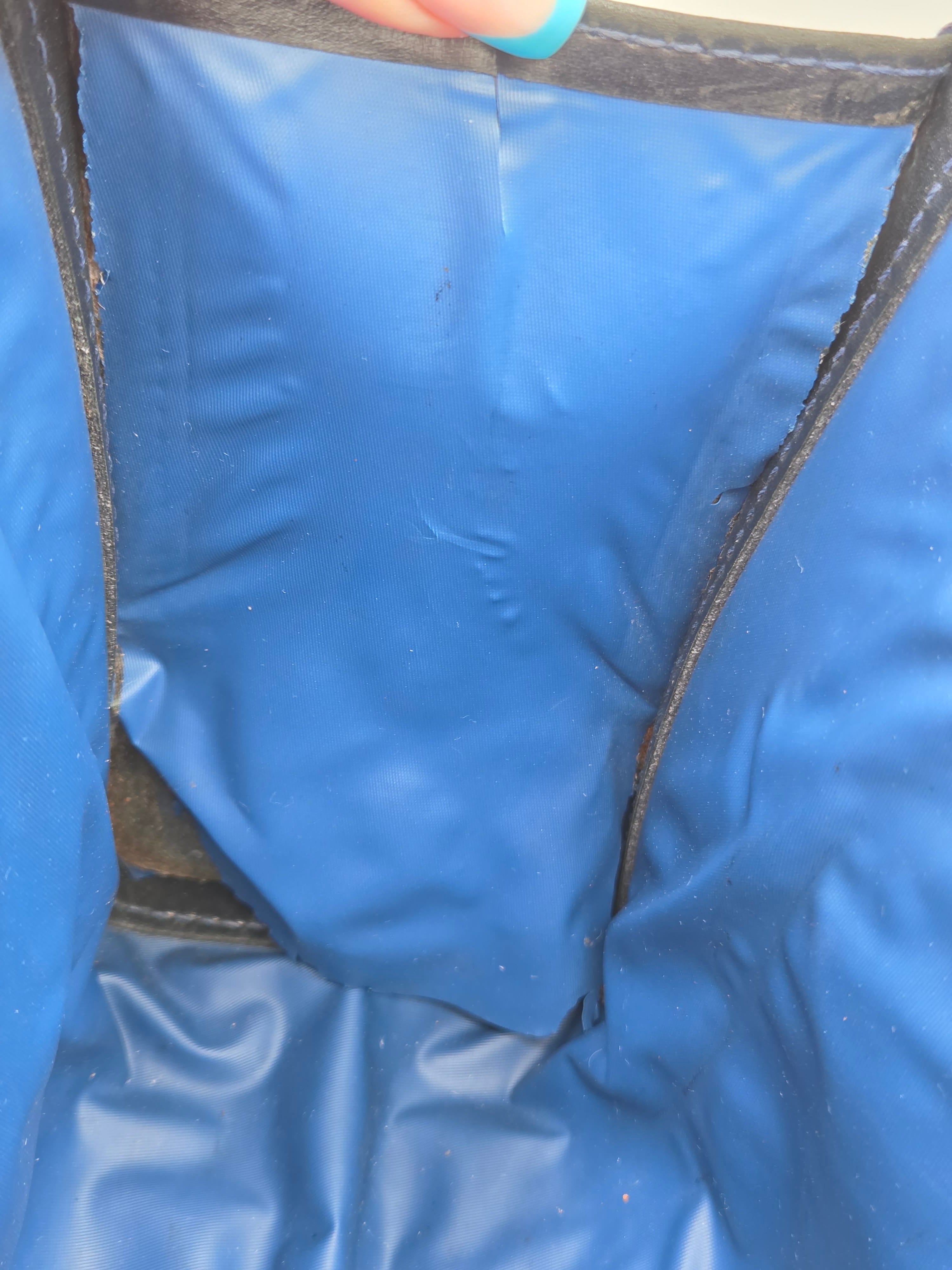 Close-up of the interior of a blue padded or waterproof bag, showing blue fabric panels and dark trim, with a small portion of a finger visible at the left edge.