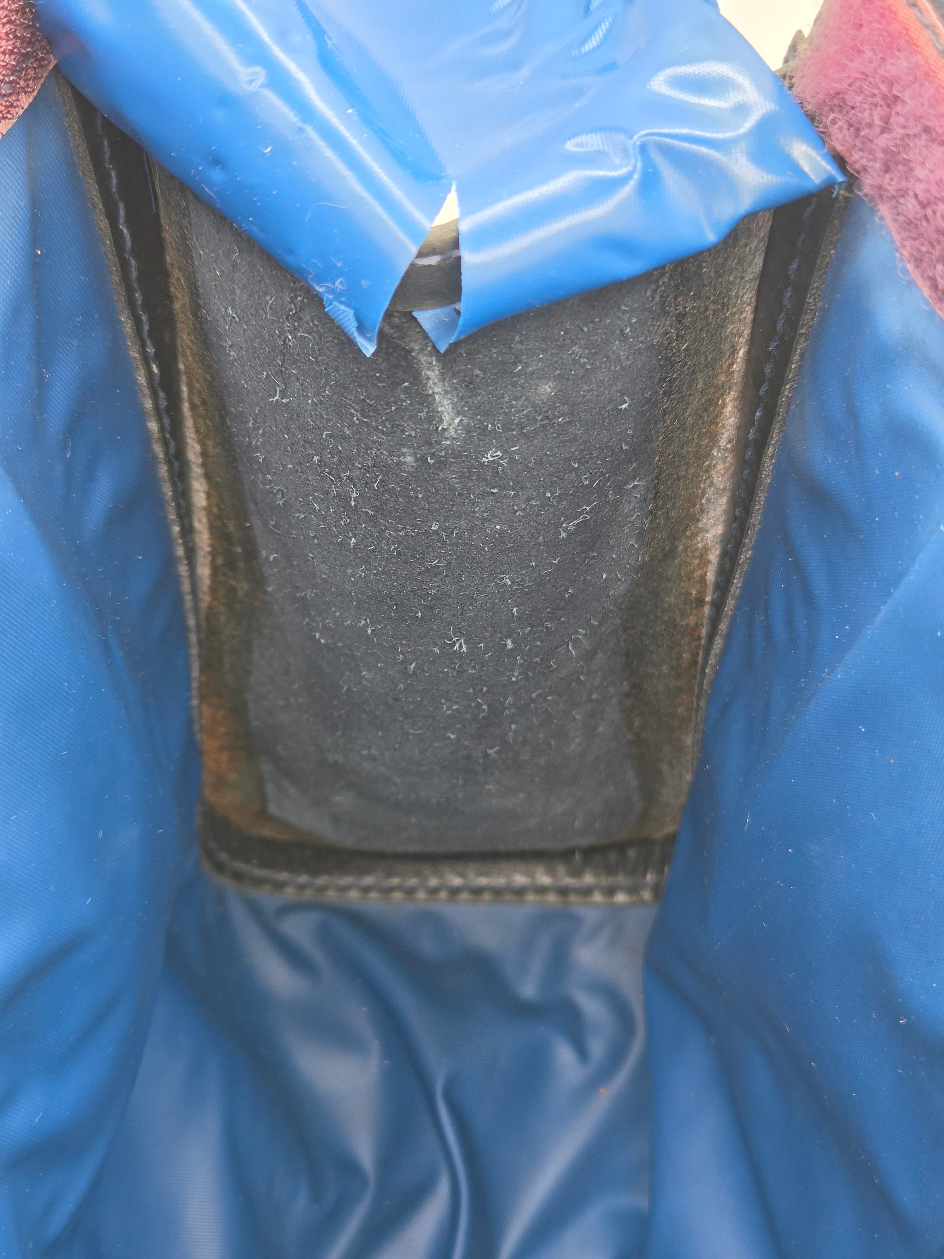 Close-up of the interior opening of a blue waterproof jacket or waterproof bag, showing a dark gray waterproof flap or liner with black stitched edges.