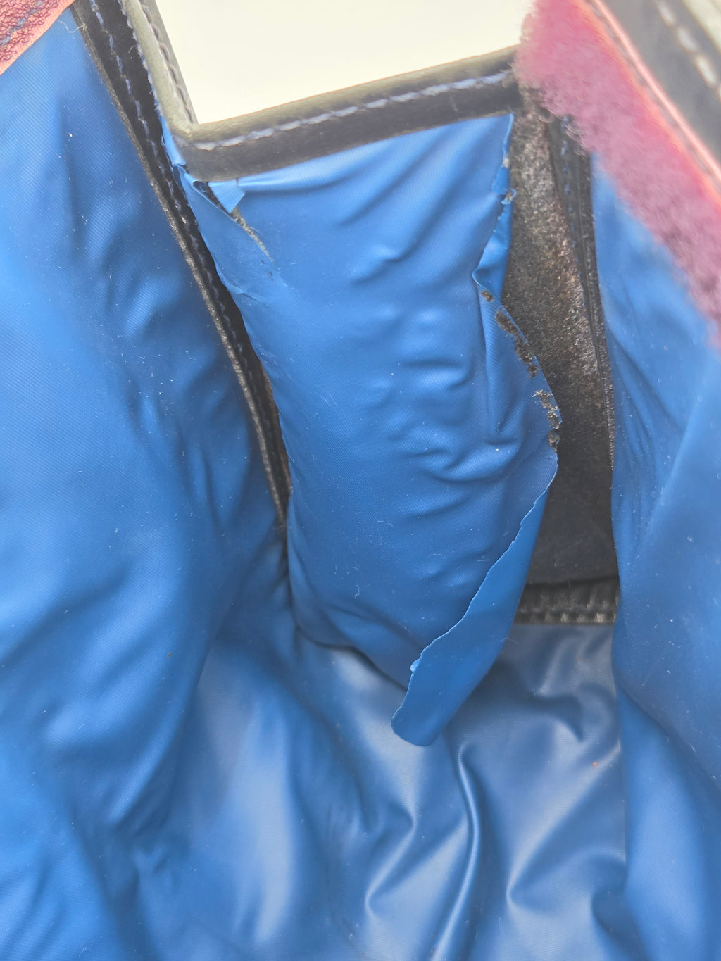 Close-up of a blue padded cushion or support inside a garment or bag, showing shiny blue fabric, dark trim, and a small portion of a pinkish fabric edge.