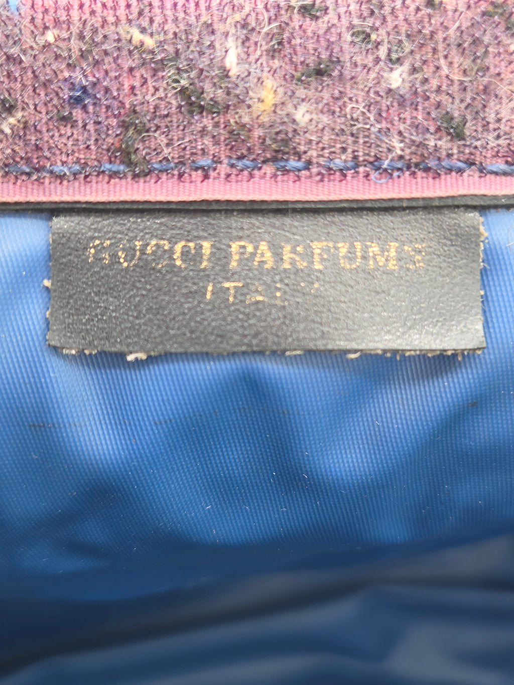Close-up of a black fabric label with gold text reading 'KOTO PARFUMS' sewn onto a blue ribbed textile, next to a pink and purple woven trim.