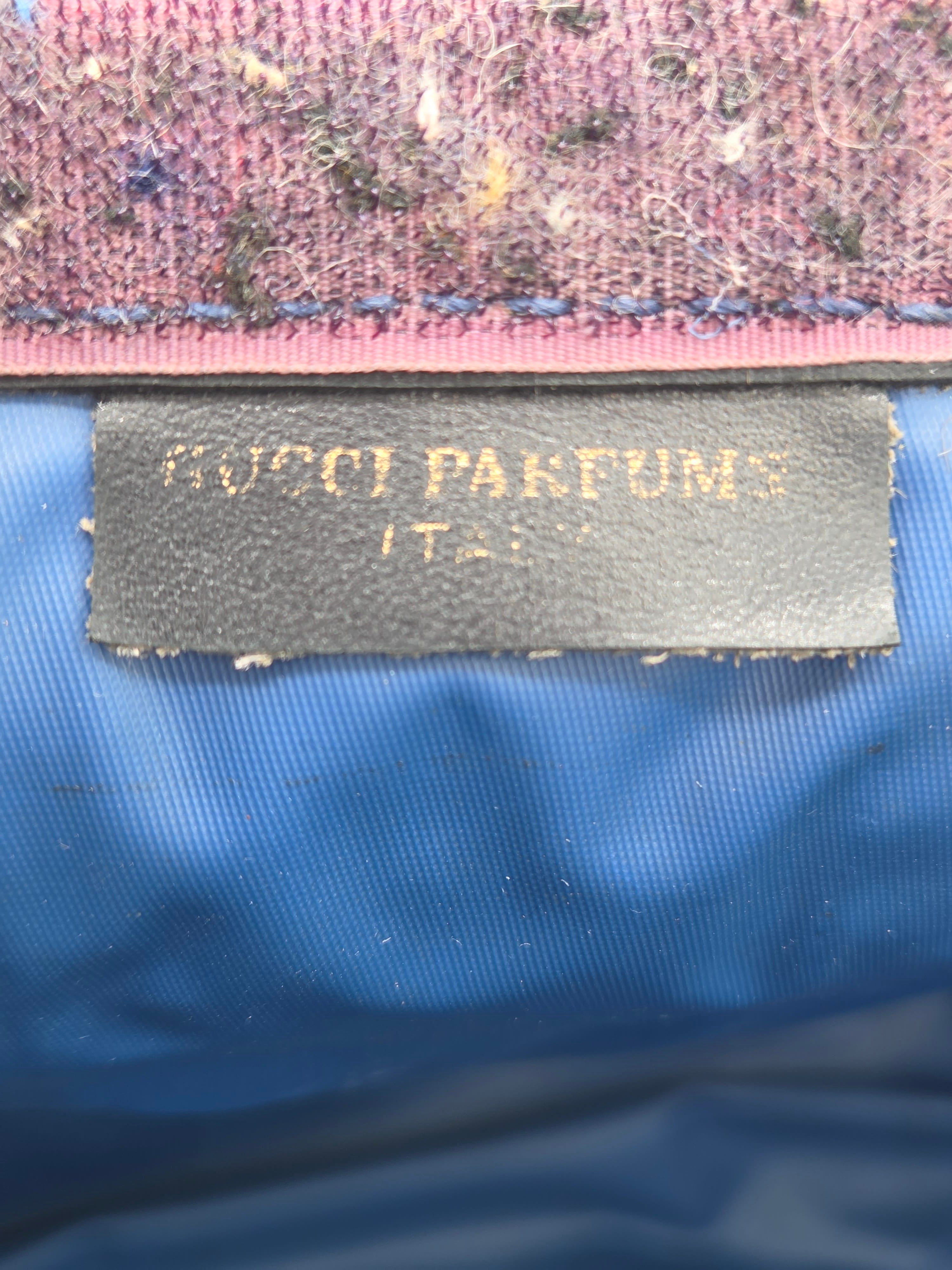 Close-up of a black fabric label with gold text reading 'KOTO PARFUMS' sewn onto a blue ribbed textile, next to a pink and purple woven trim.
