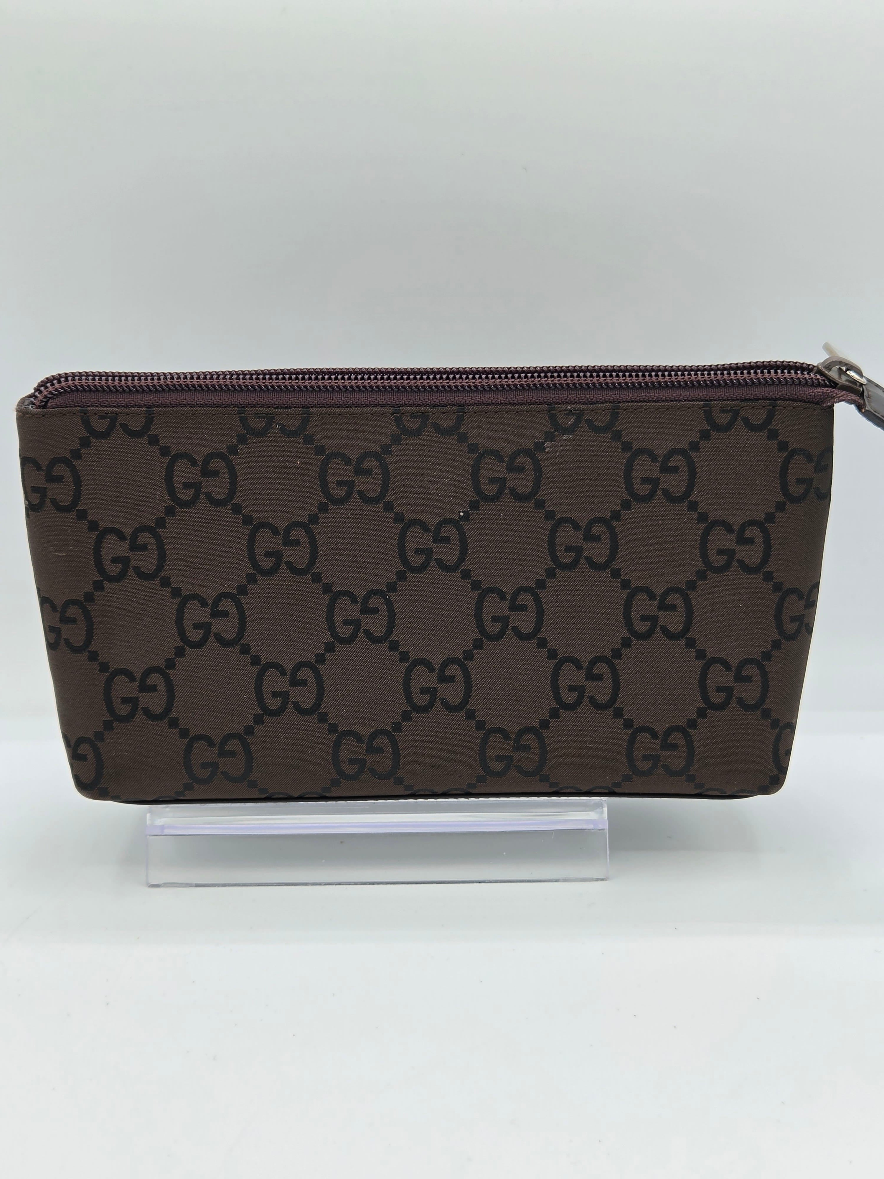 A brown monogram zip-around pouch with a repeating interlocking G pattern, shown standing upright against a plain white background.