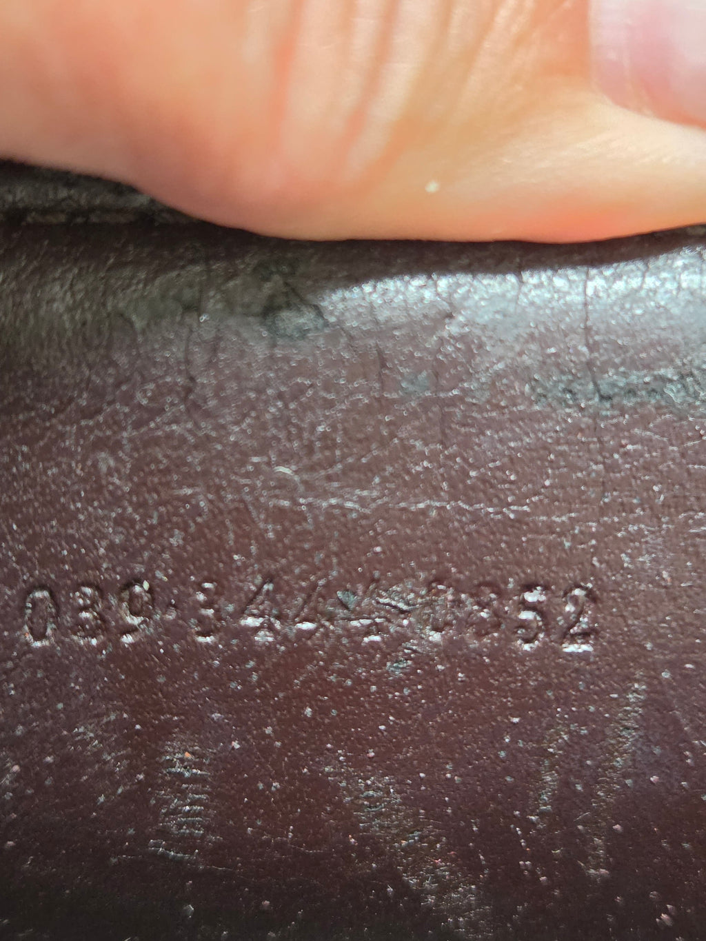 Close-up of a dark brown textured leather surface with embossed numbers and a finger pressing down at the top edge.