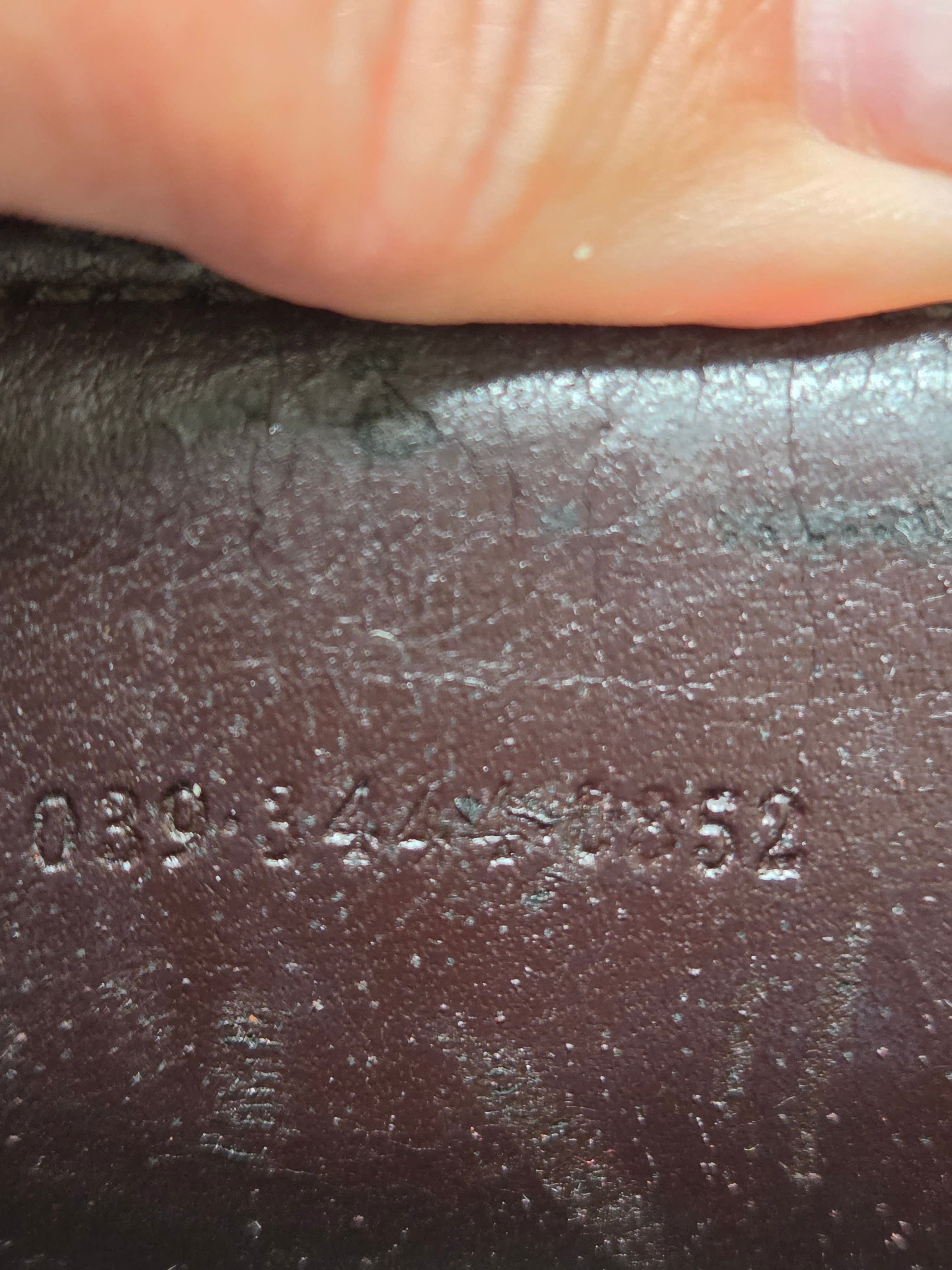 Close-up of a dark brown textured leather surface with embossed numbers and a finger pressing down at the top edge.