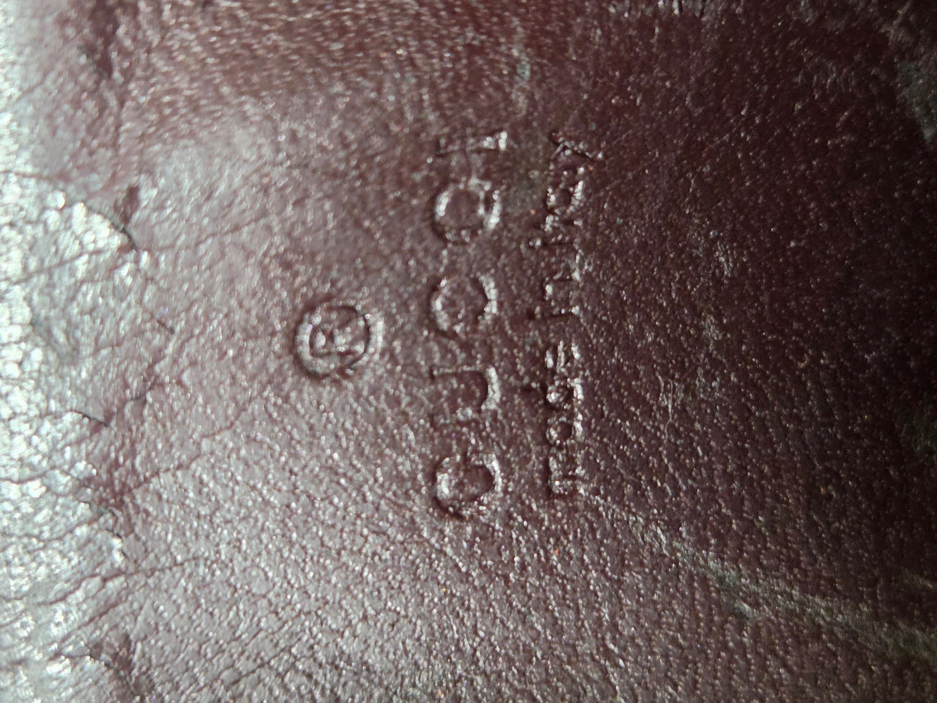 Close-up of embossed leather texture with a circular logo and vertical text reading 'Gucci Made in Italy' on a dark brown leather surface.