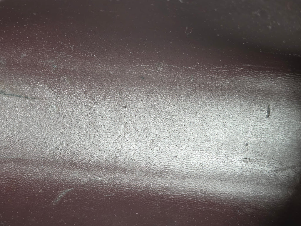 A close-up view of a dark brown textured leather surface with a horizontal seam and visible scuffs and scratches.