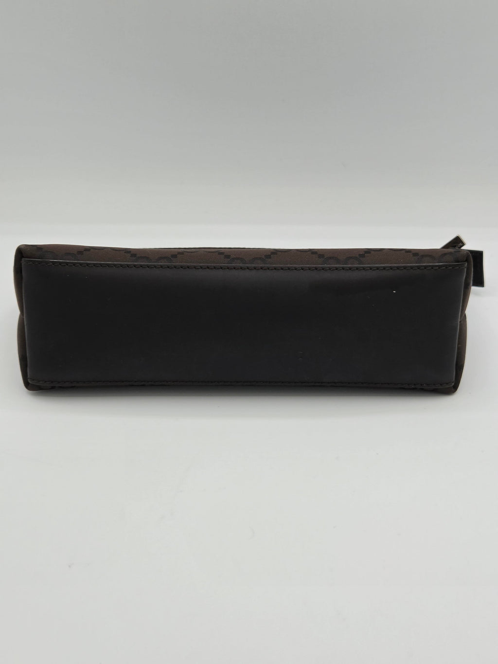 A dark brown leather pouch with a subtle monogram pattern, shown vertically against a plain light gray background.