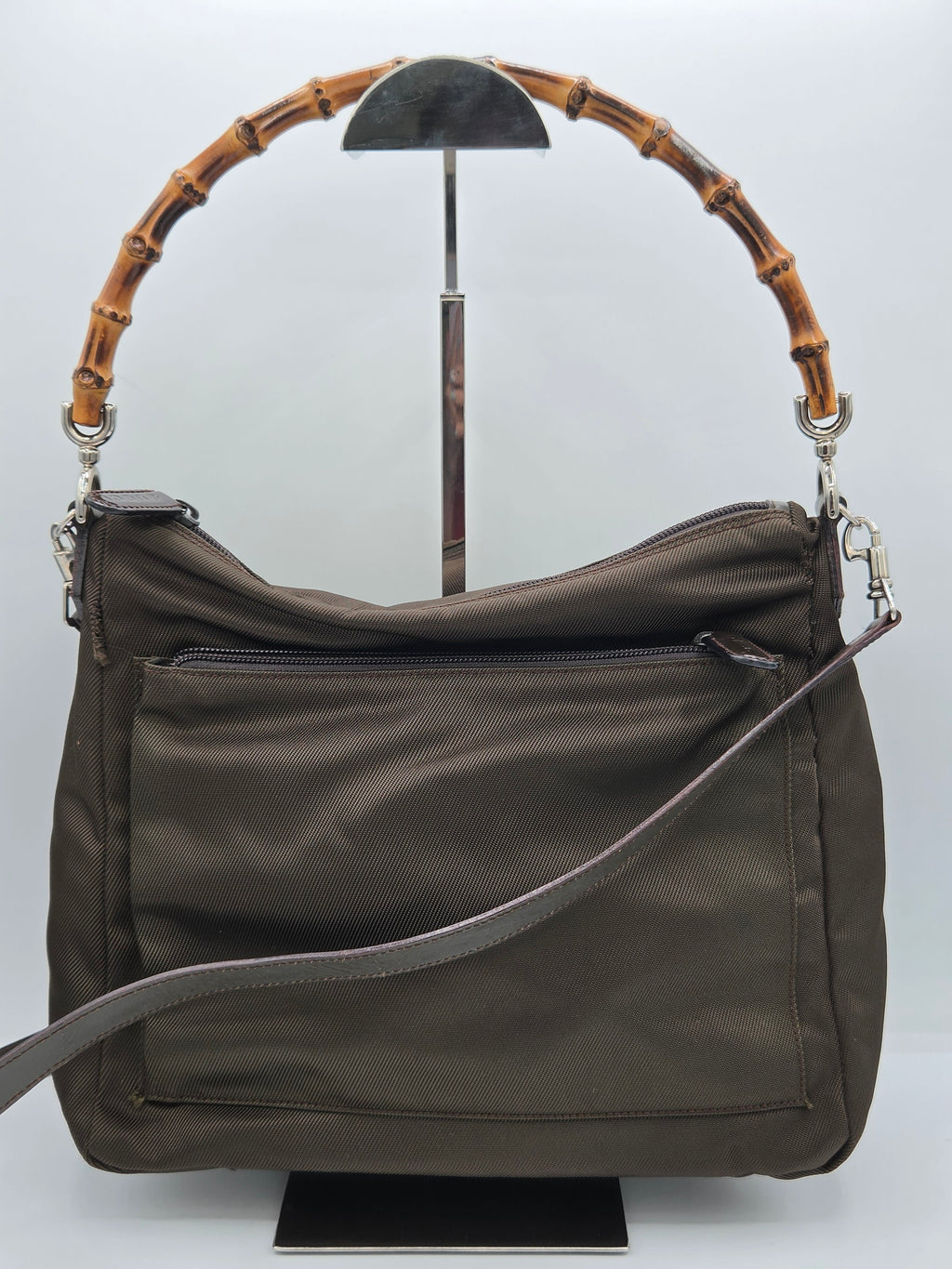 An olive green nylon shoulder bag with a distinctive curved bamboo handle and a gray adjustable strap, displayed on a white background.
