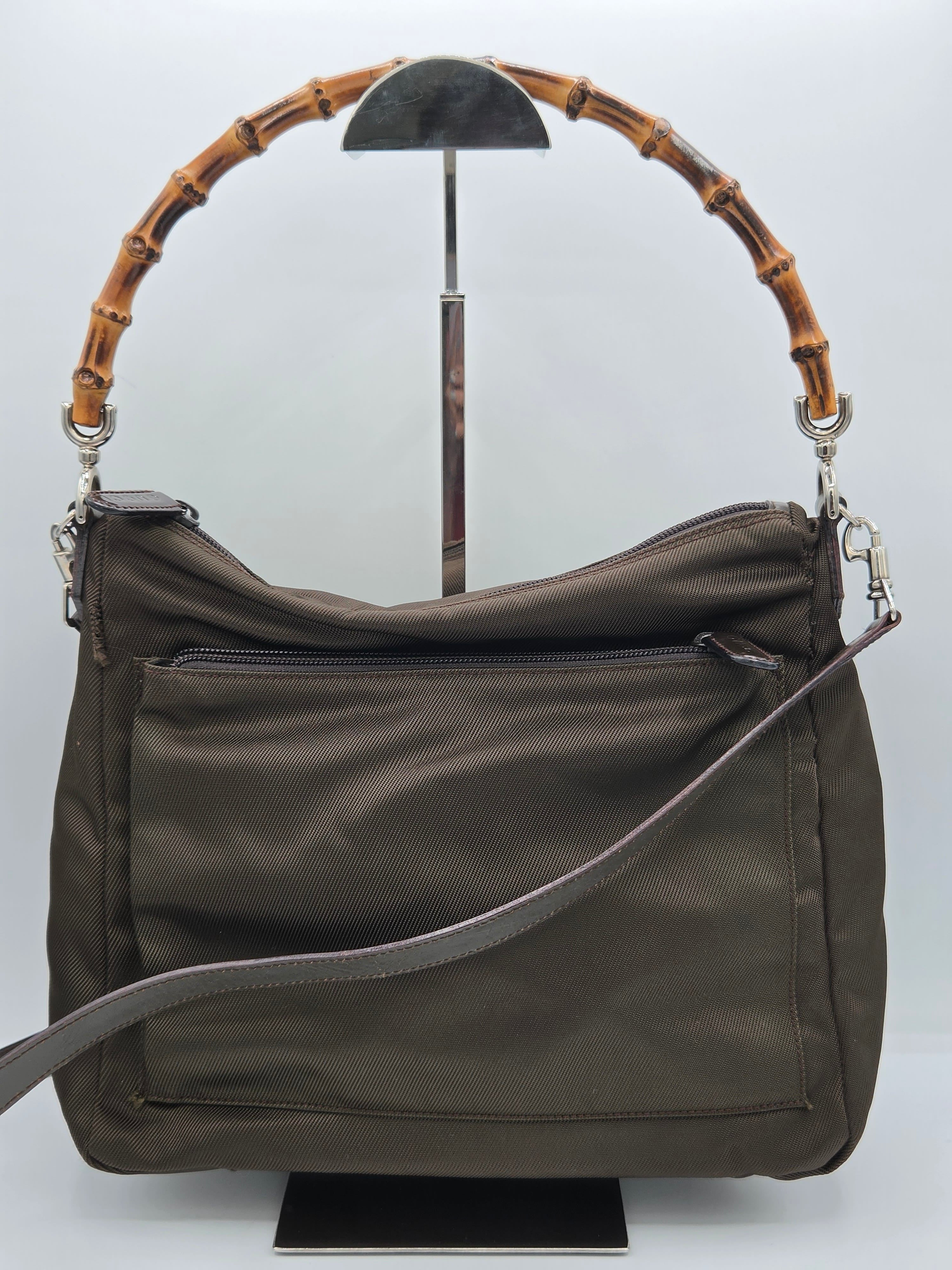 An olive green nylon shoulder bag with a distinctive curved bamboo handle and a gray adjustable strap, displayed on a white background.