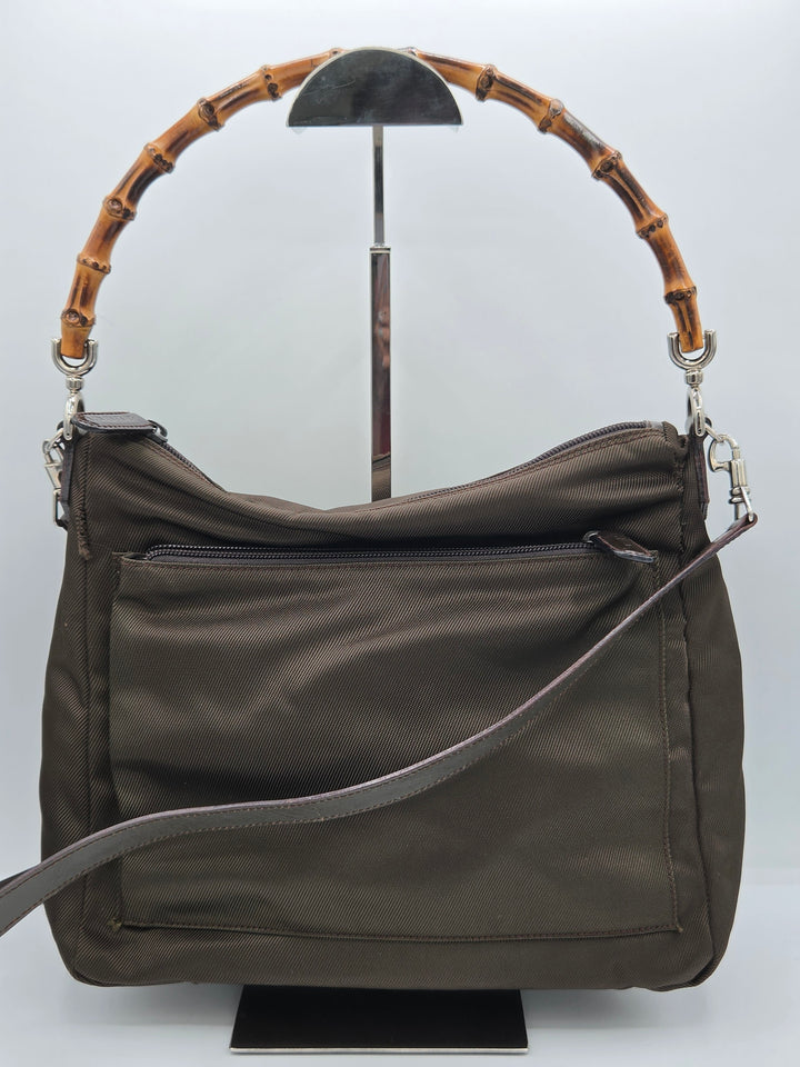 An olive green nylon shoulder bag with a distinctive curved bamboo handle and a gray adjustable strap, displayed on a white background.