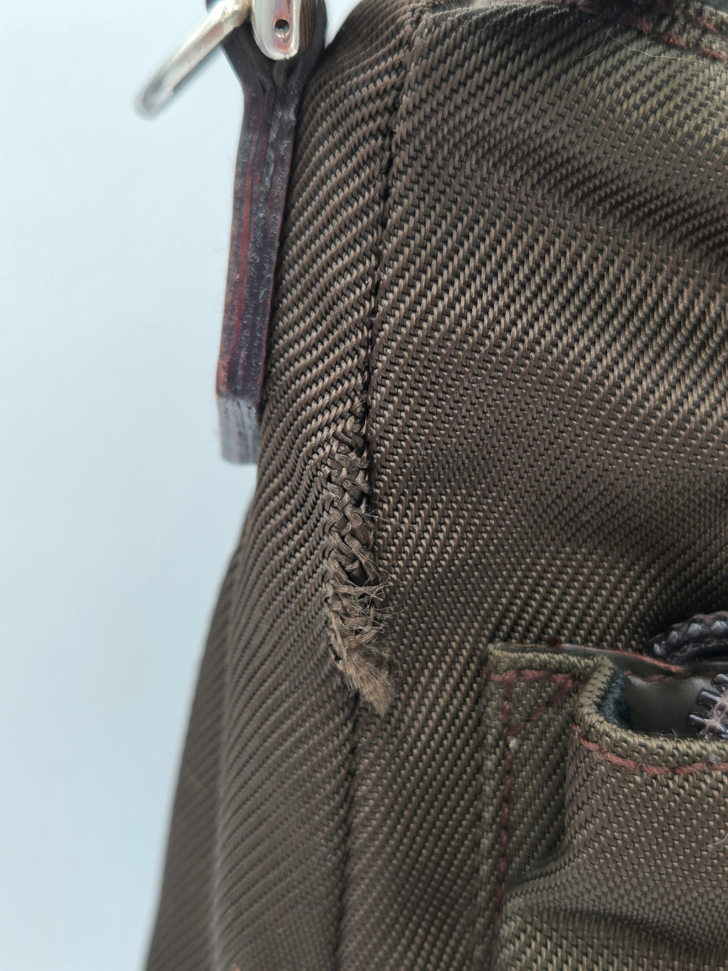 Close-up of a dark olive green canvas bag showing a frayed, loose stitch near the zipper tab.