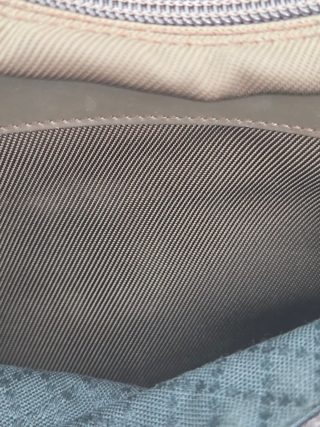 Close-up detail of a fabric item showing a dark gray woven strap or panel, a beige stitched edge, and a light blue patterned textile.