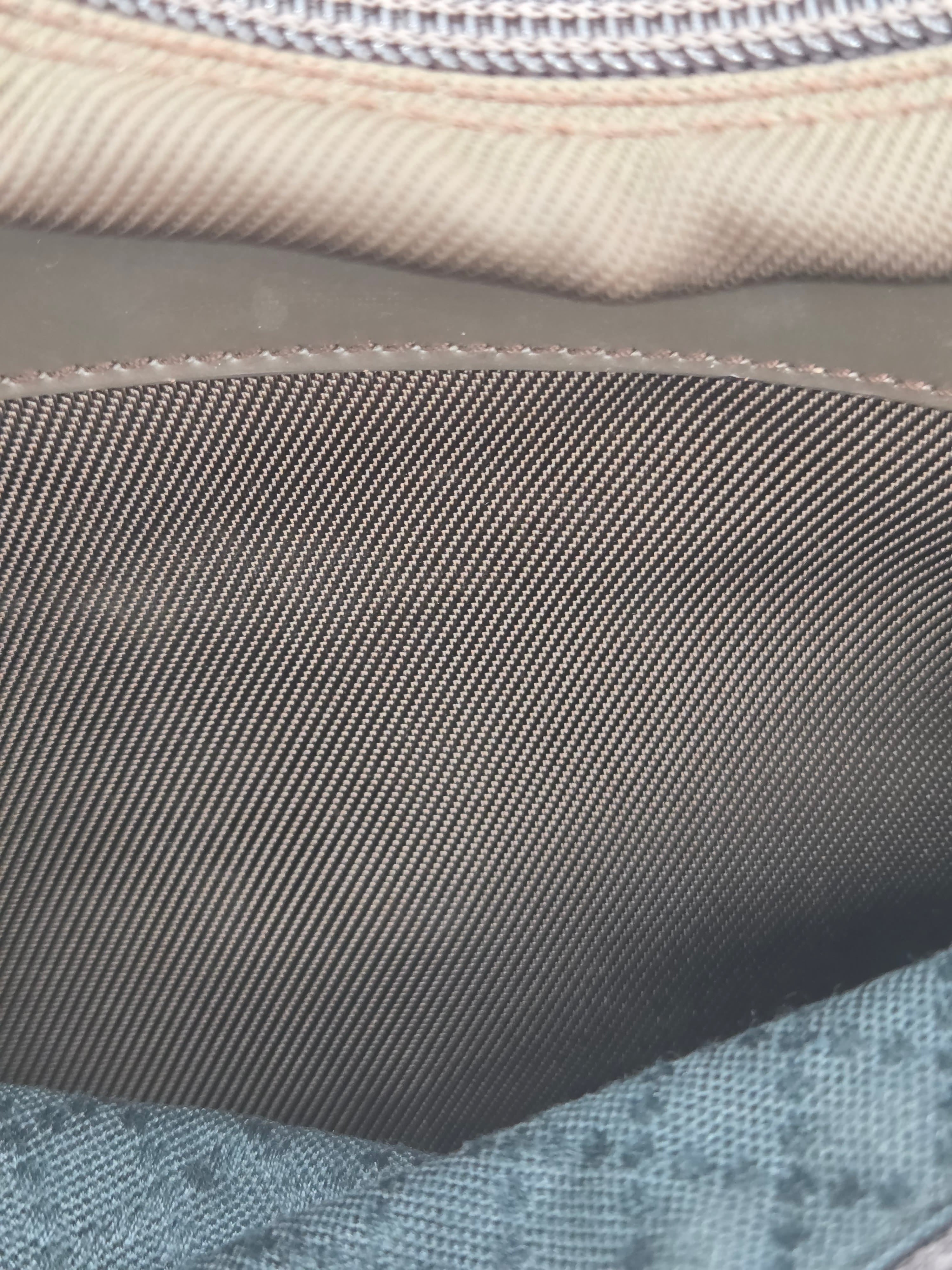 Close-up detail of a fabric item showing a dark gray woven strap or panel, a beige stitched edge, and a light blue patterned textile.