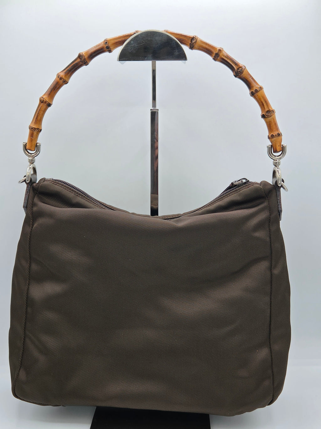 A dark brown shoulder bag with a distinctive curved bamboo handle, displayed on a white background.
