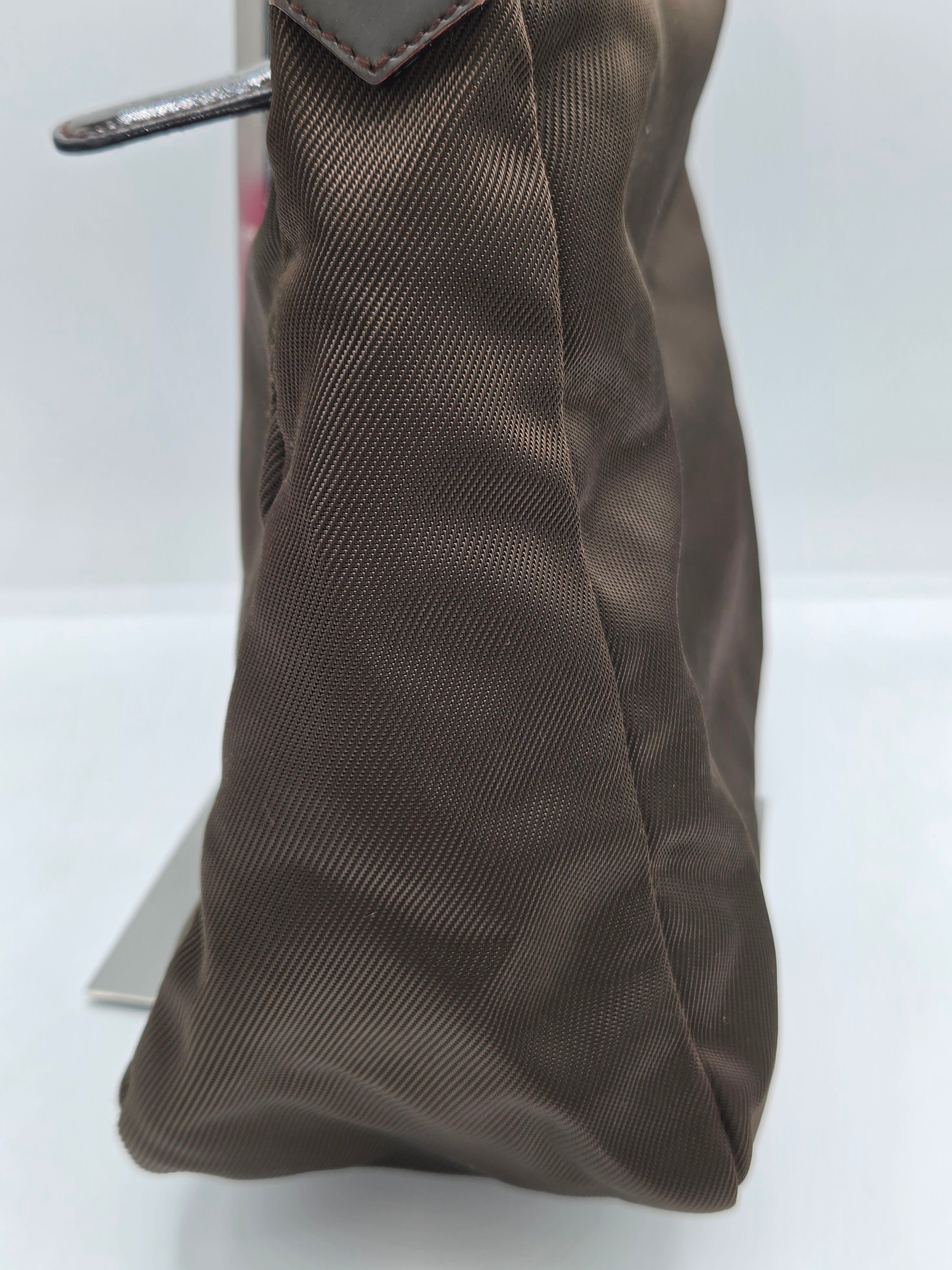 A close-up of a dark brown nylon or canvas pouch with a textured diagonal weave pattern, featuring a silver metal zipper pull on the left side.