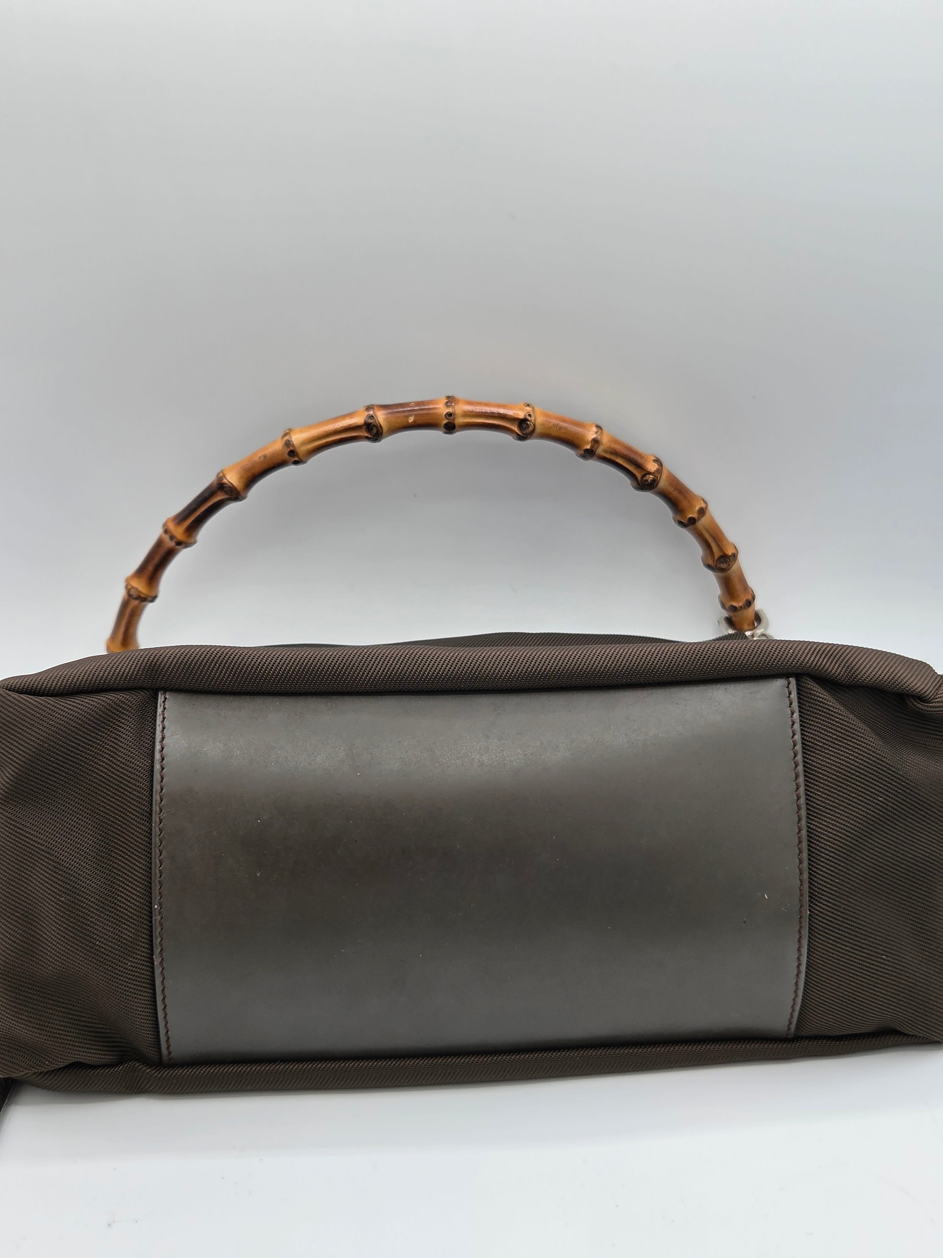 A dark brown fabric handbag with a smooth dark brown leather panel on the front and a distinctive curved bamboo handle, shown against a plain light gray background.
