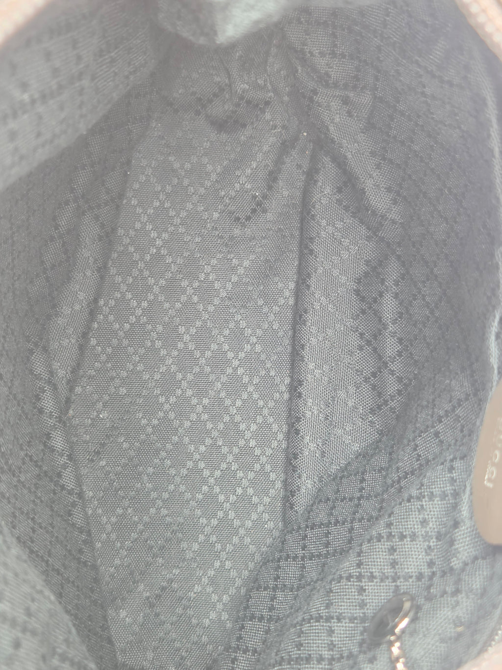 Close-up of the interior lining of a handbag, showing a gray and white patterned fabric with a zipper pull and a small brand tag visible at the top.