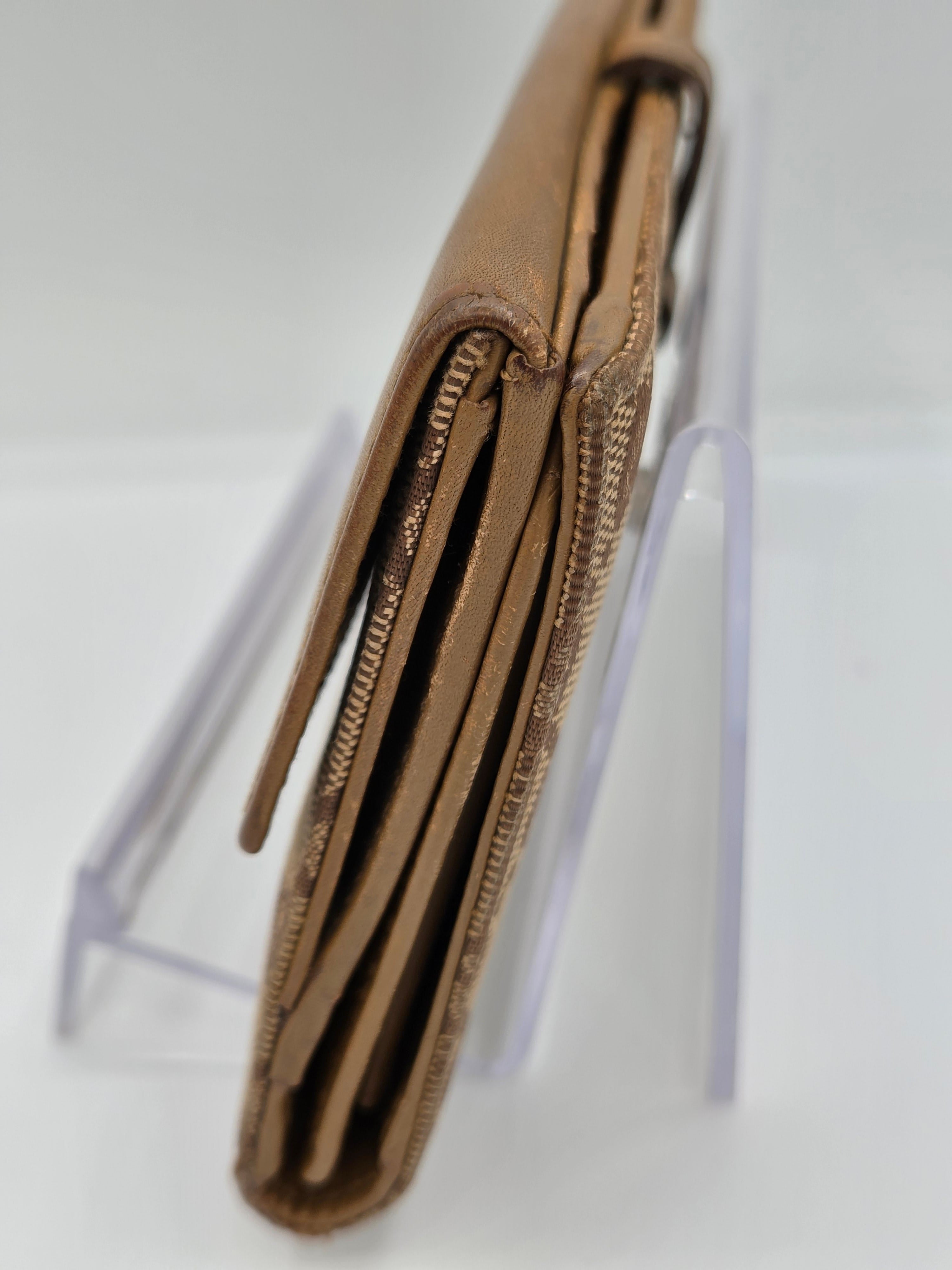 A close-up of a tan leather wallet or clutch with multiple zippered compartments, displayed on a clear acrylic stand against a white background.