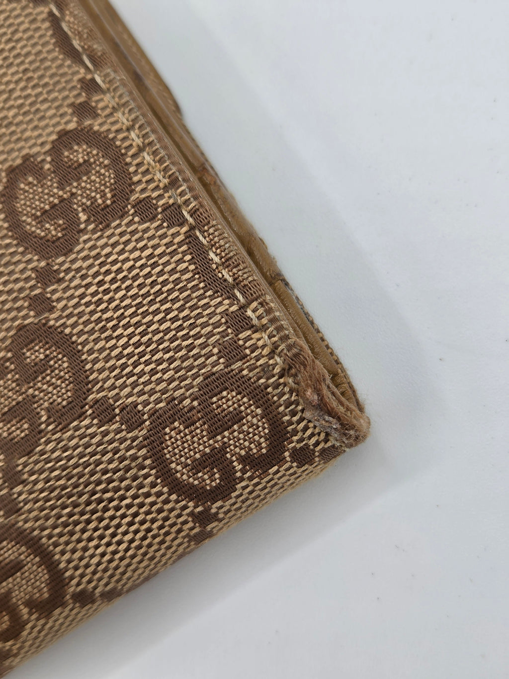 Close-up of a beige and brown monogram canvas item, showing the textured woven pattern and a rolled corner on a white background.