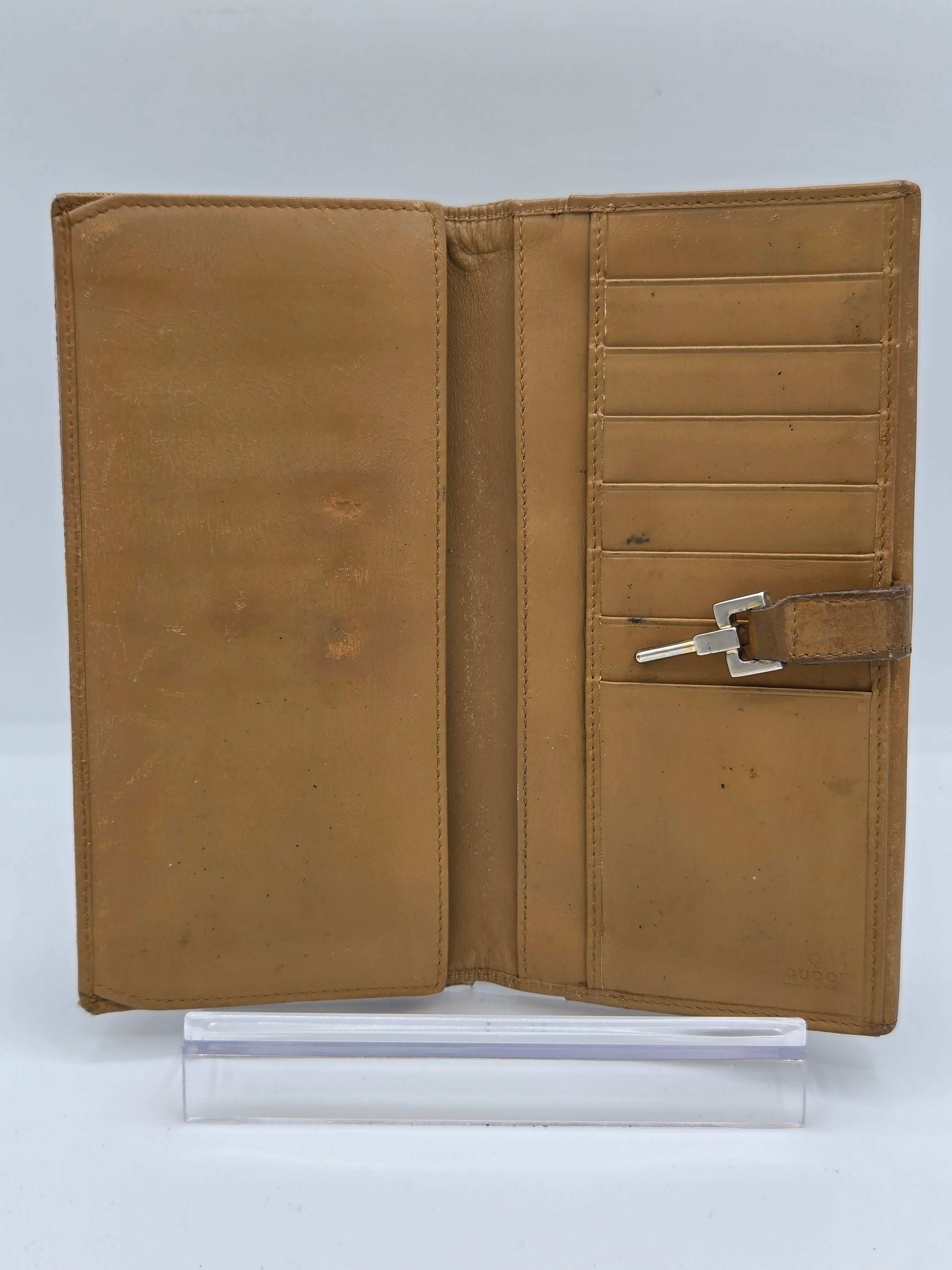 A tan leather wallet shown open, featuring multiple card slots, a central keyhole pocket with a silver key, and a large slip pocket below. A clear plastic sleeve is positioned to the right of the wallet on a white background.