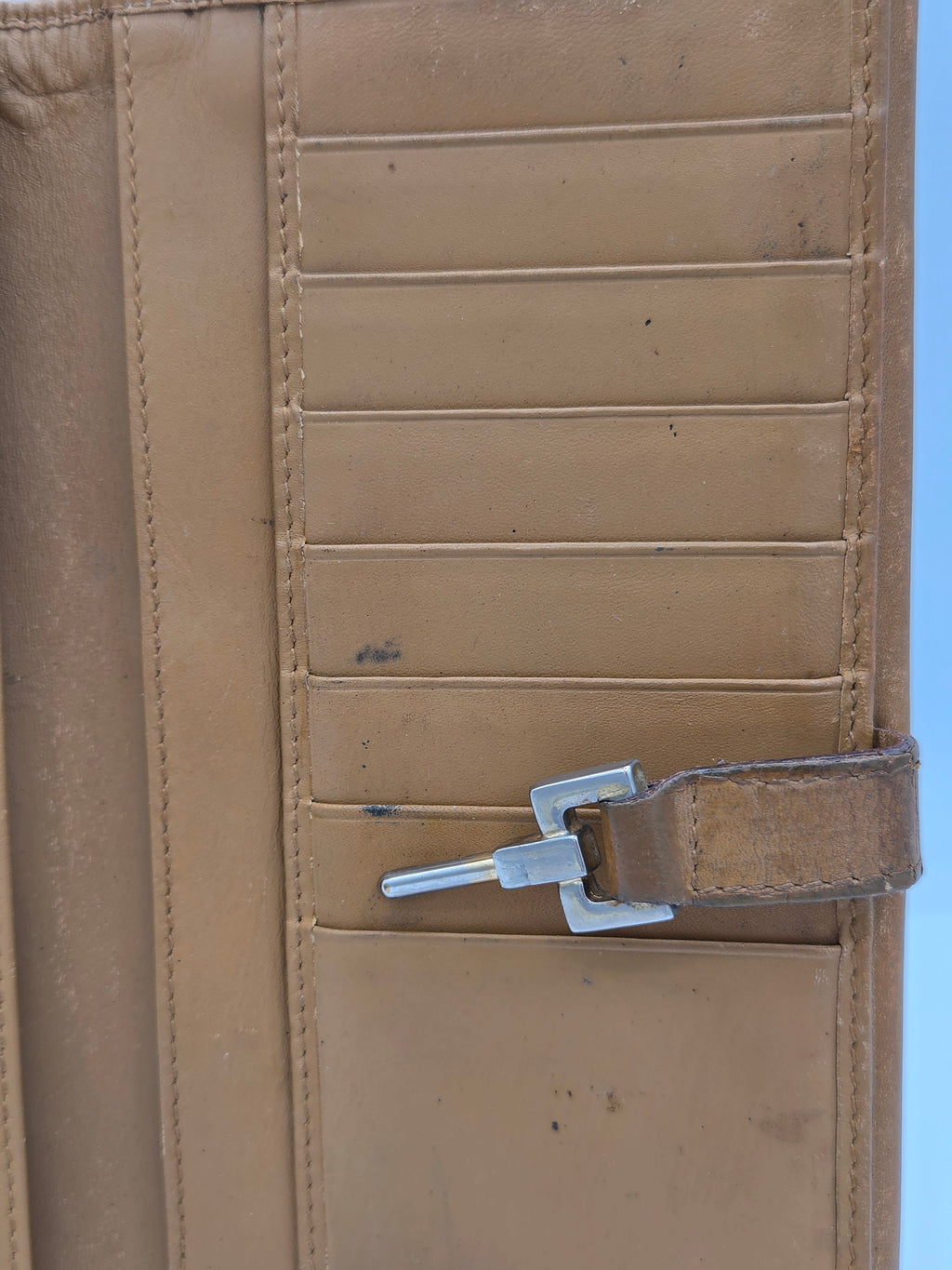 Close-up of a tan leather or faux-leather accessory with multiple vertical card slots, a horizontal stitched band, and a silver metal clip or hook fastened to the top edge.