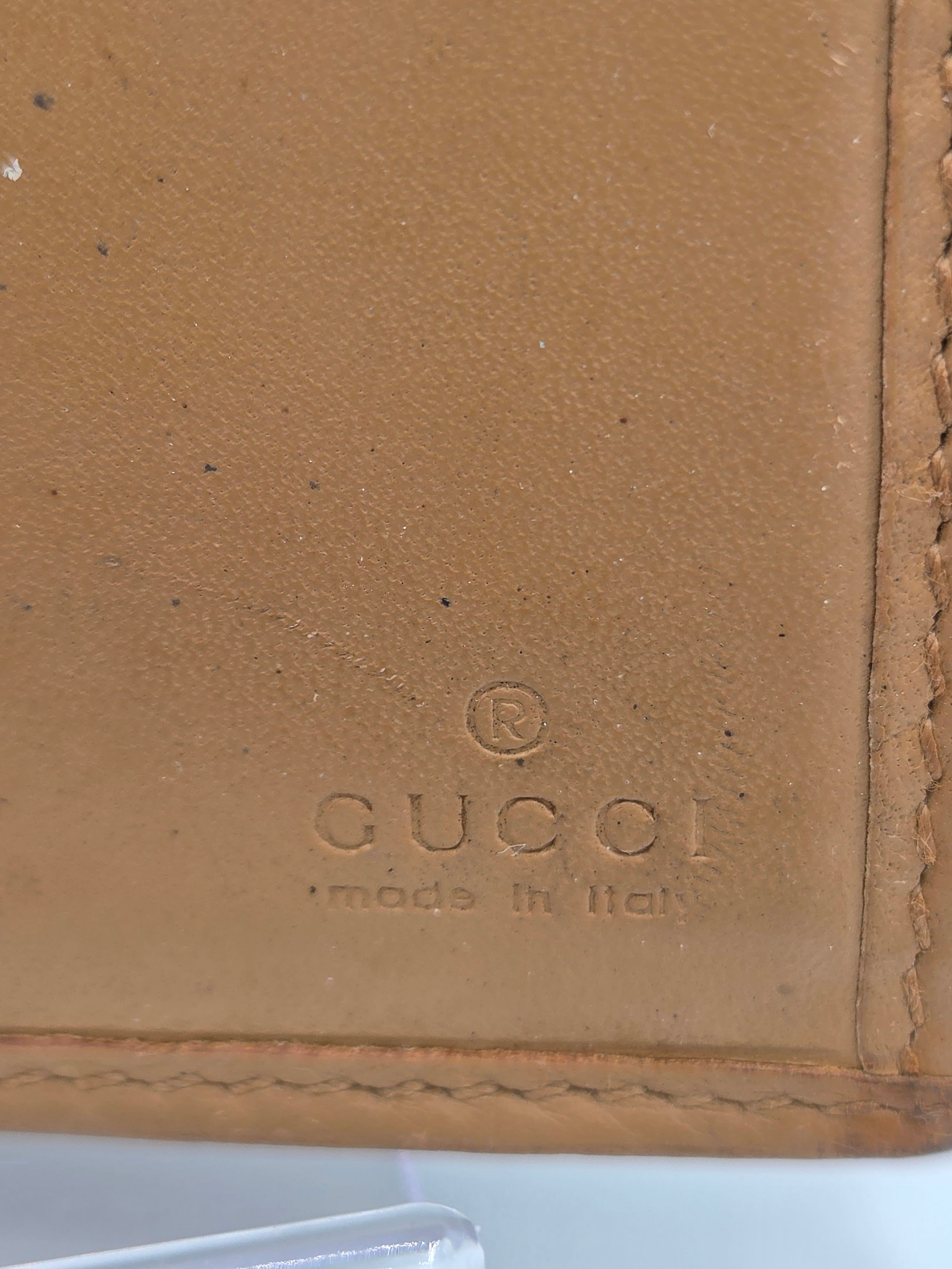 Close-up of a tan leather wallet corner with visible Gucci branding embossed on the surface and stitched edges.