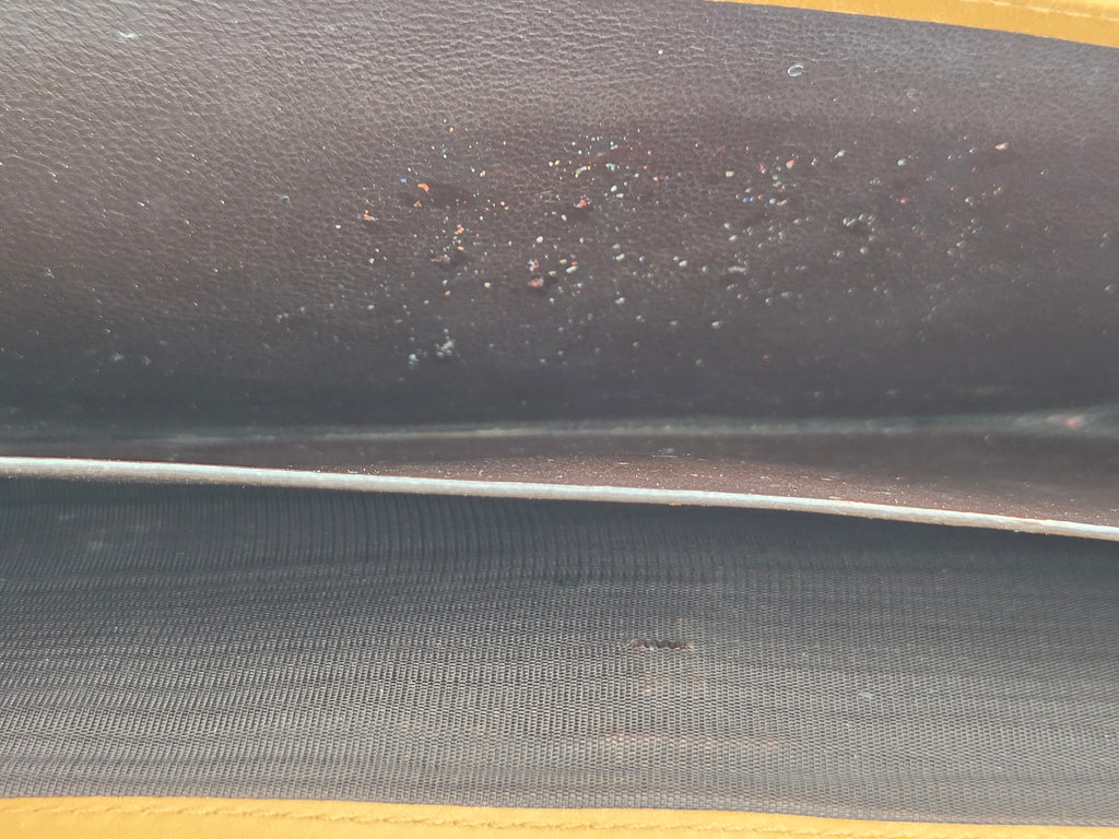 Close-up of a dark brown textured leather interior panel with small scattered specks and a visible seam, alongside a dark gray ribbed fabric section.