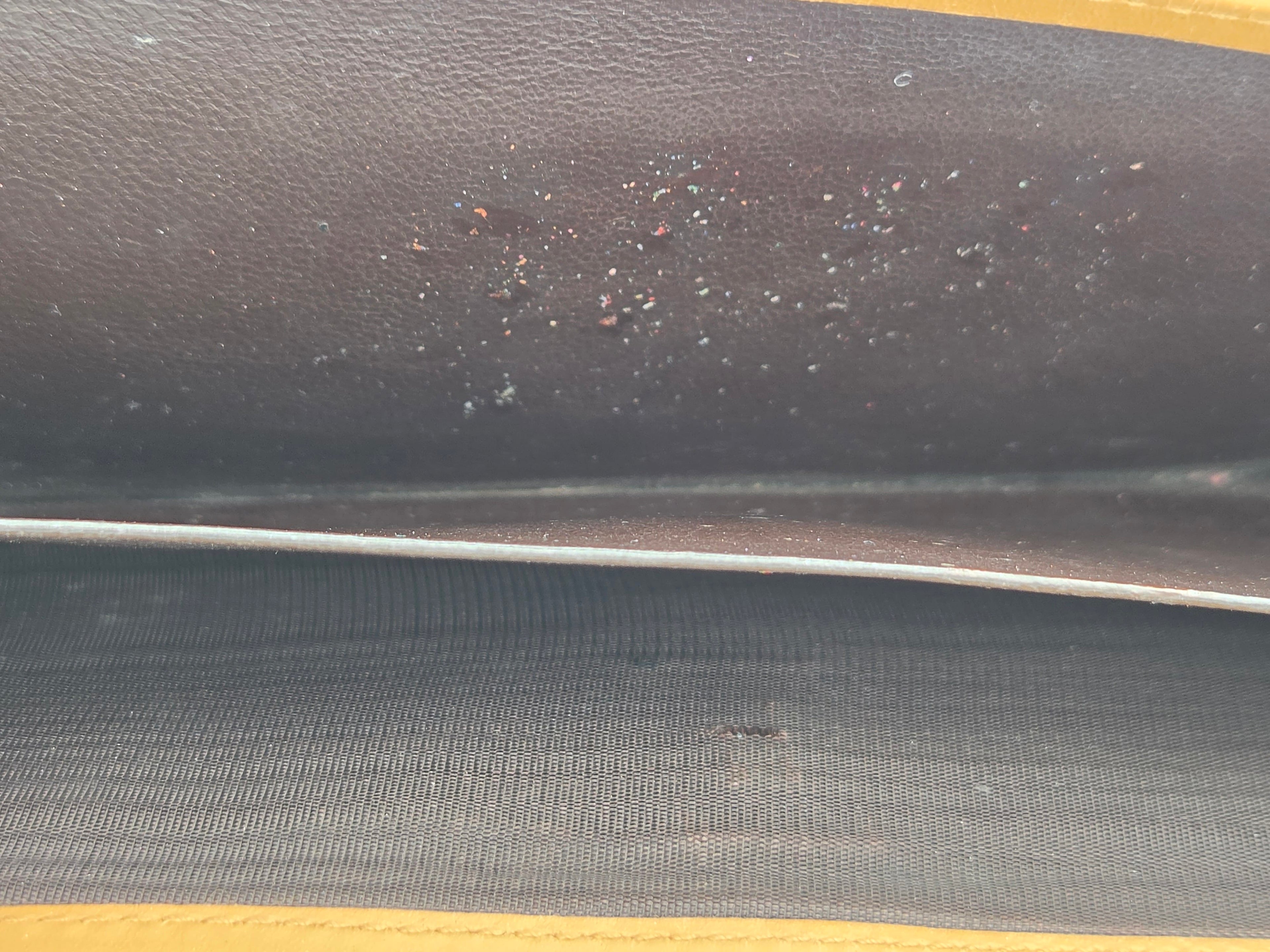 Close-up of a dark brown textured leather interior panel with small scattered specks and a visible seam, alongside a dark gray ribbed fabric section.