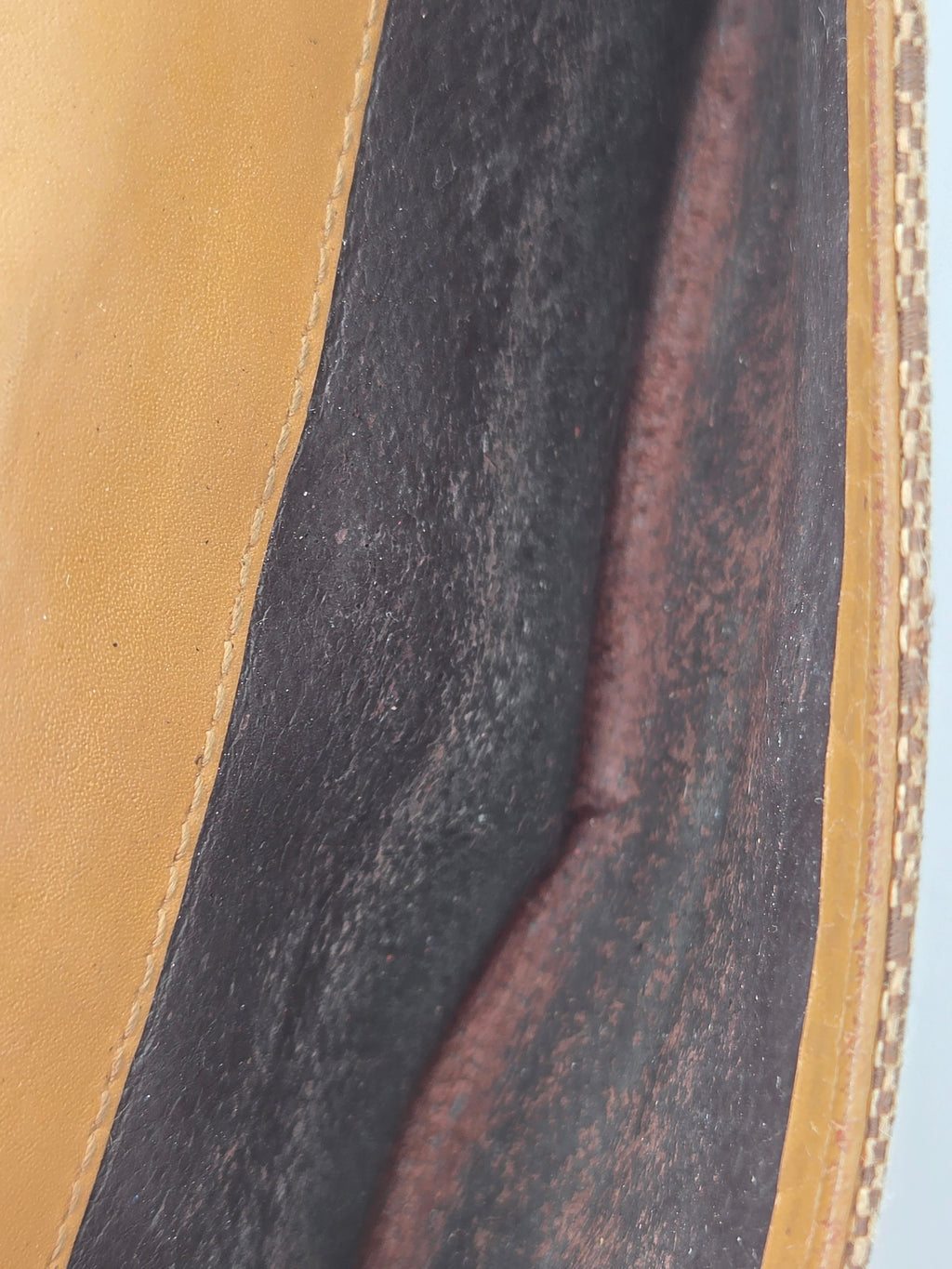 Close-up detail of a leather bag showing a dark charcoal textured interior panel bordered by tan leather trim.
