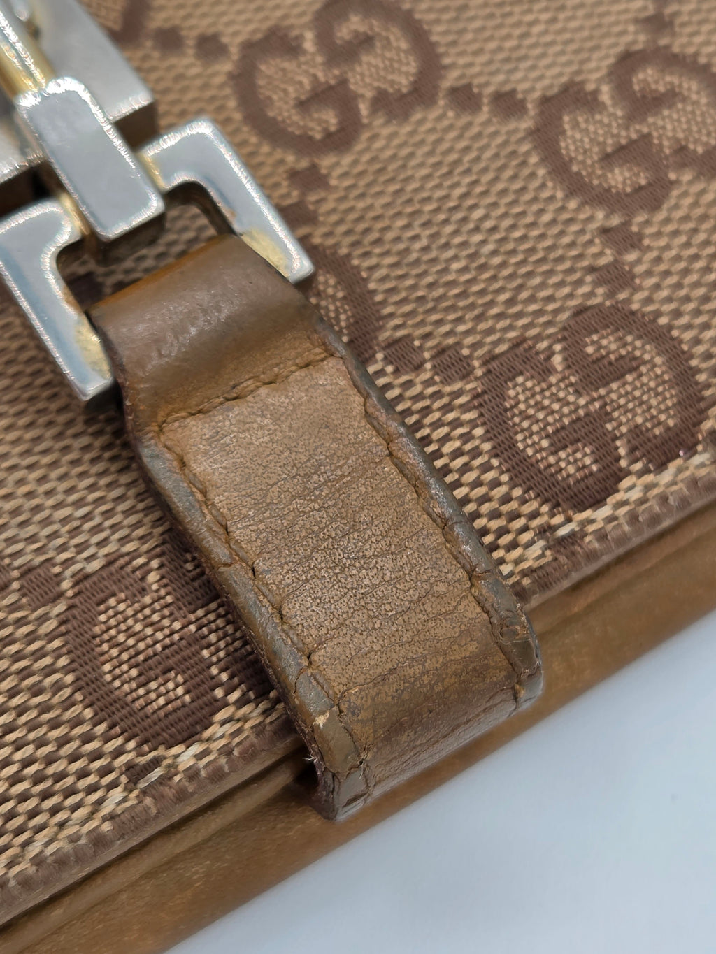 Close-up of a beige and brown monogram canvas bag with a brown leather strap and silver metal hardware, showing the Gucci-style interlocking G pattern.